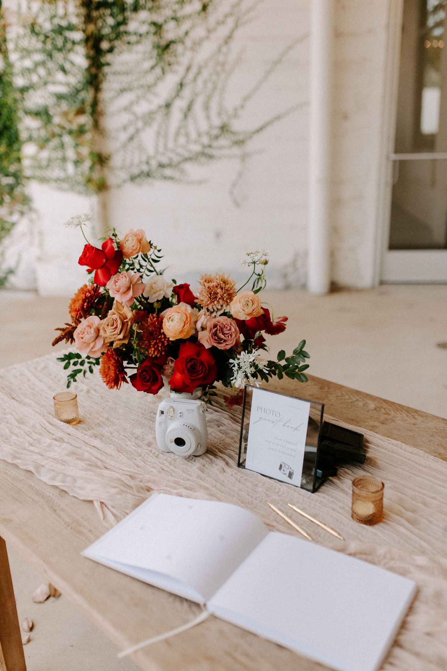 Guest book setup with red and pink floral centerpiece on wooden table with candles.