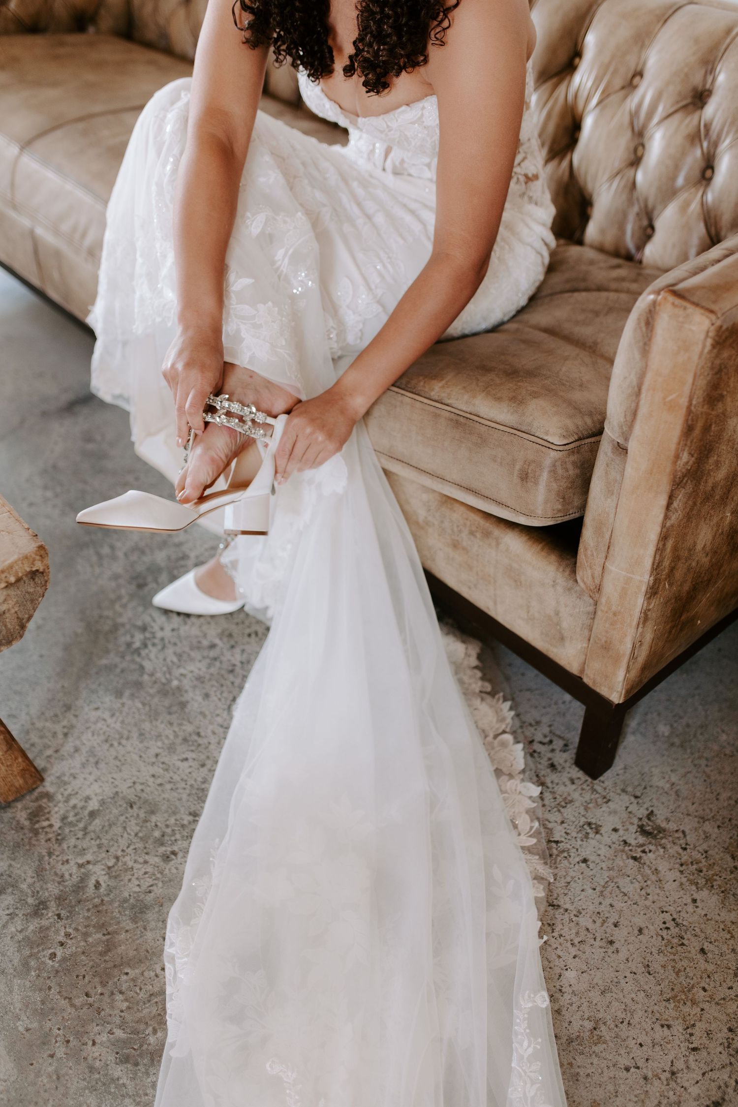 Detail shot of a wedding dress and shoes on a vintage tufted couch.