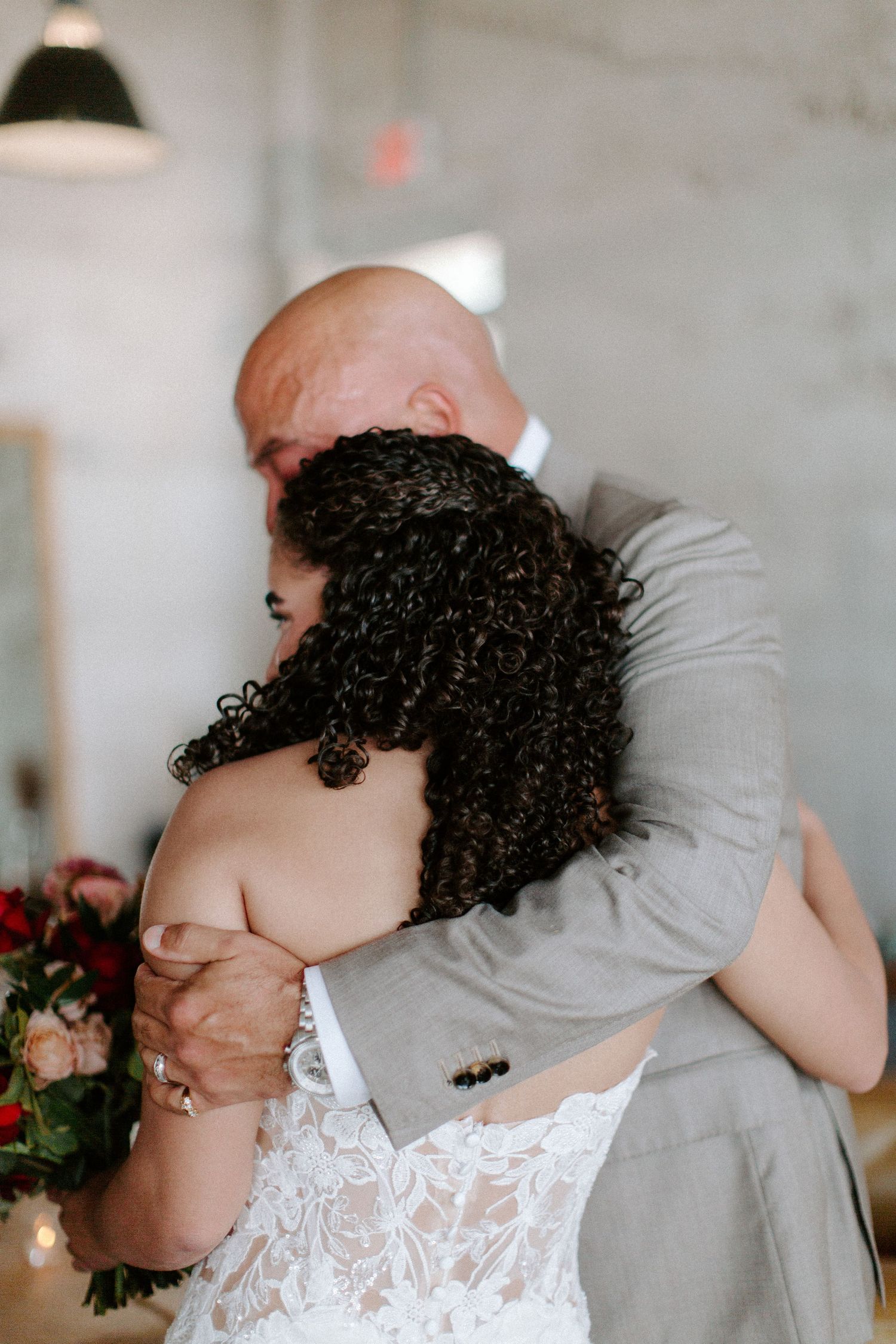 A romantic embrace between a couple in wedding attire, with curly hair and a gray suit visible.