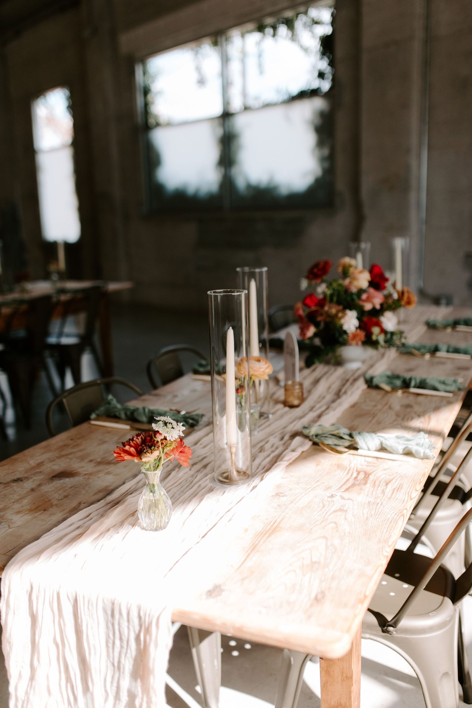 Wedding reception table with glass candleholders and white runner in natural light.