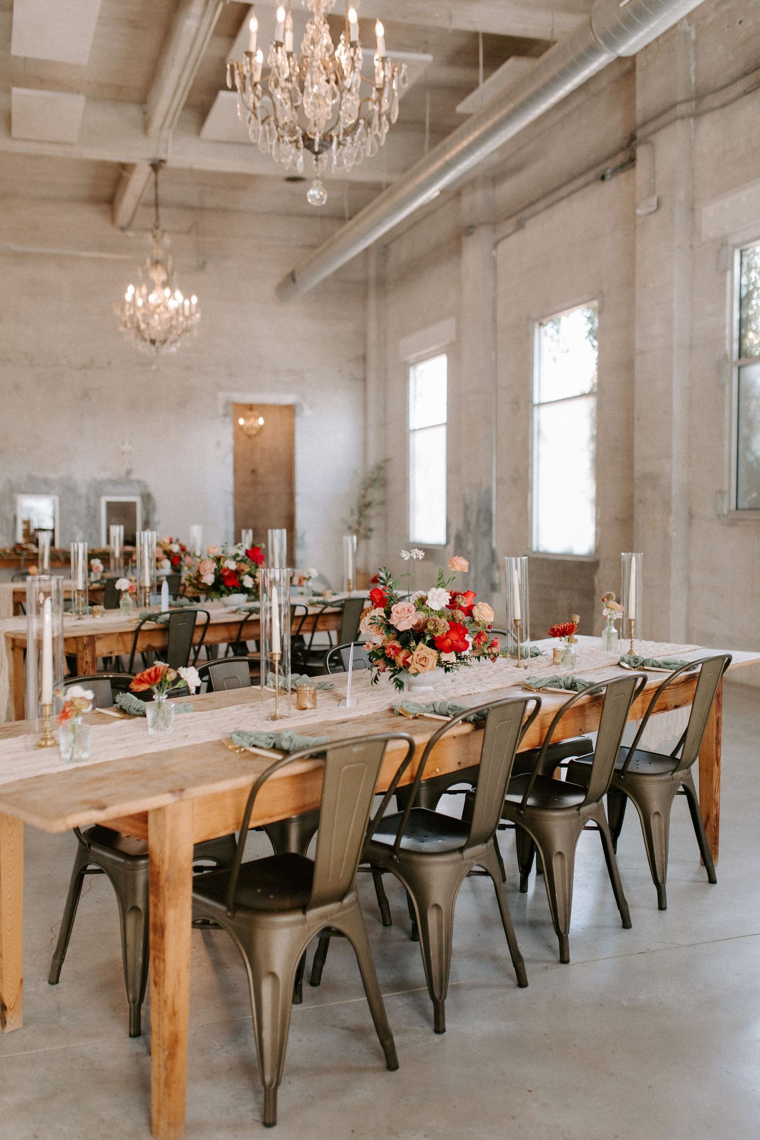 Elegant wedding reception table with industrial chairs and crystal chandeliers in an open space.