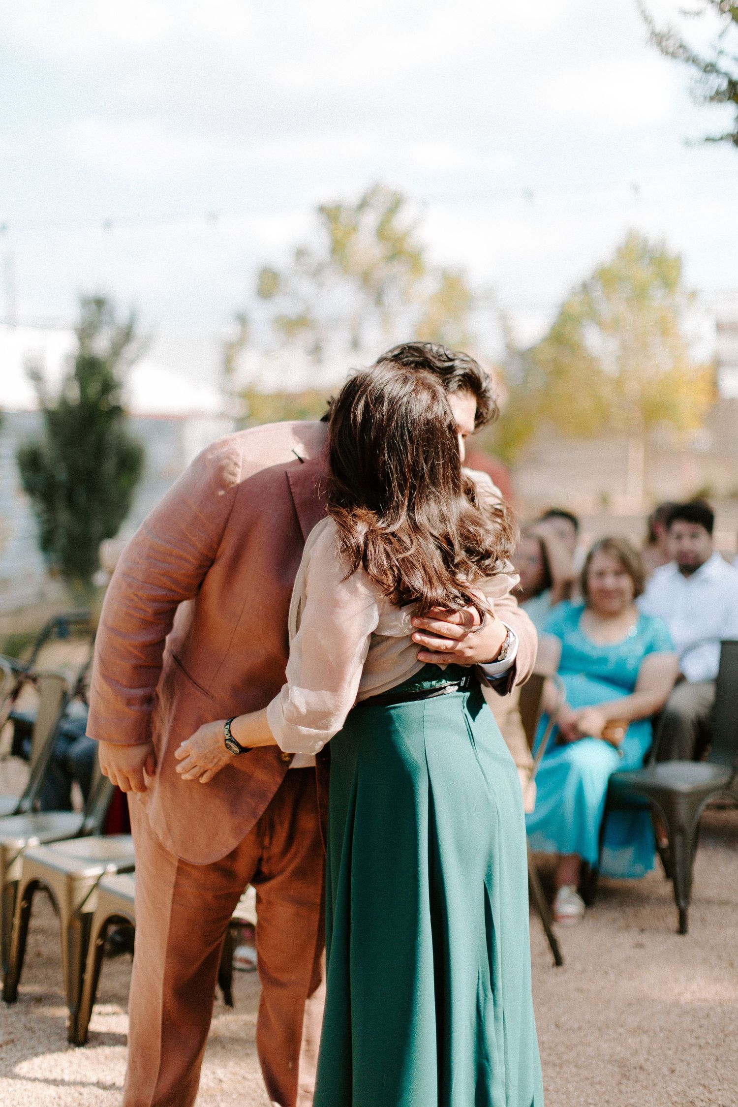 A tender moment between couple in dusty rose and emerald green attire at outdoor wedding ceremony.