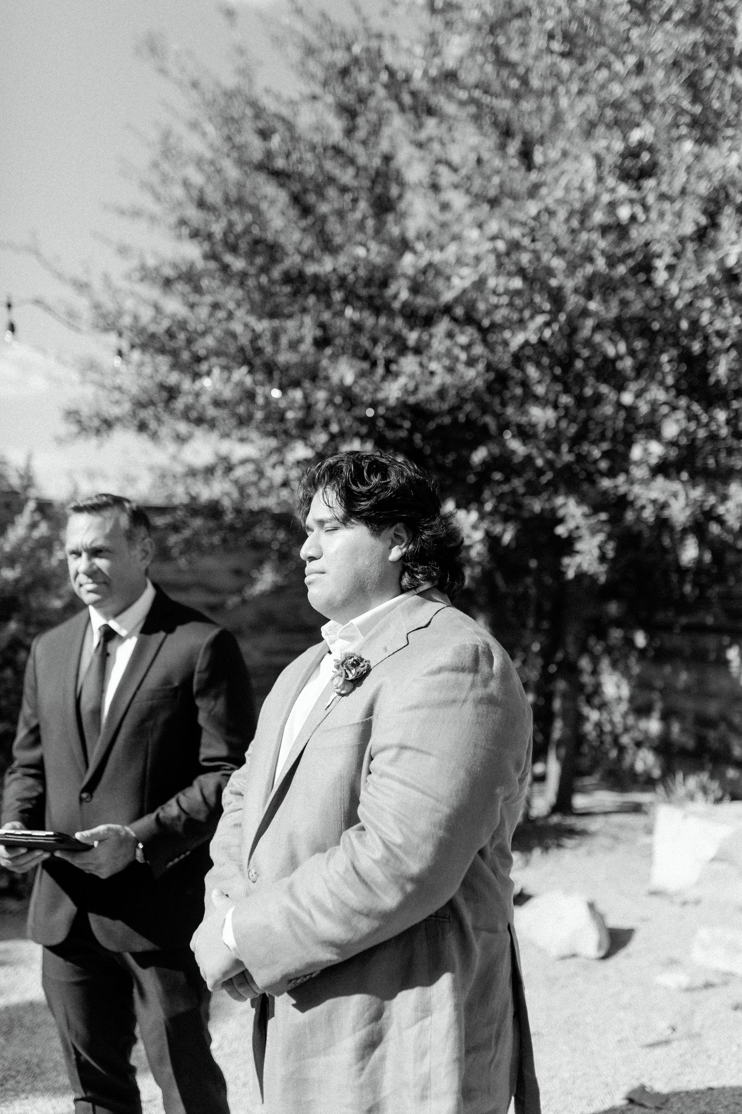 A black and white portrait of two people standing outdoors during a wedding ceremony.