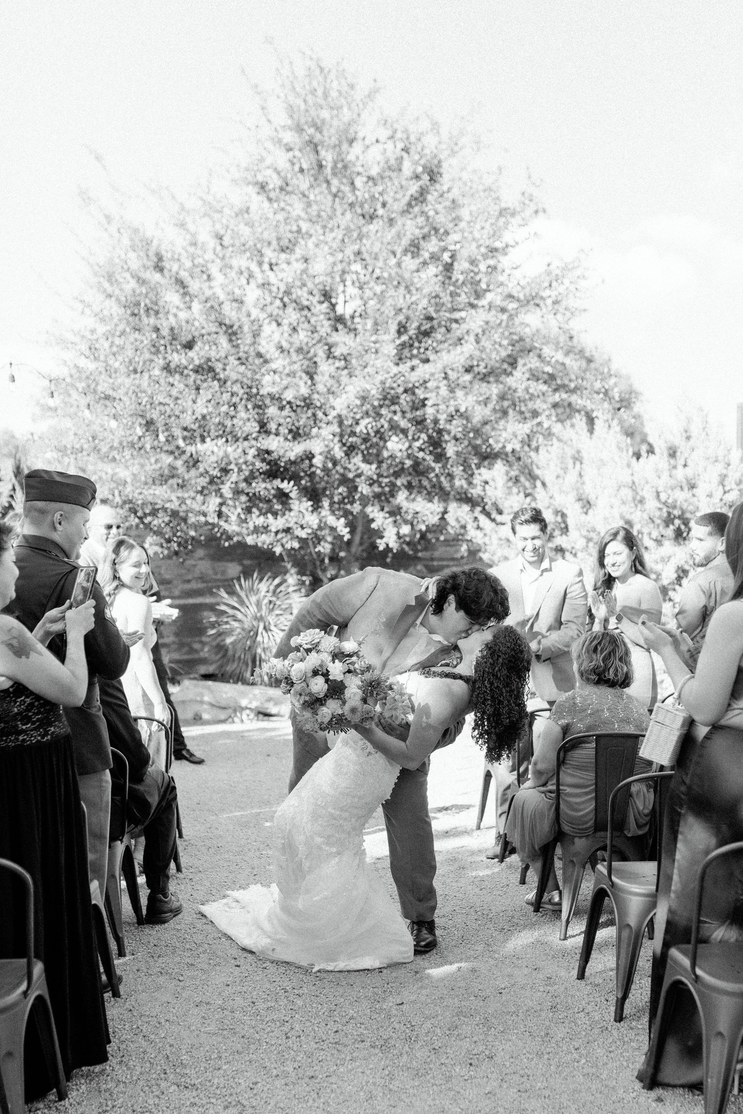 A romantic black and white photo of a wedding kiss during an outdoor ceremony.