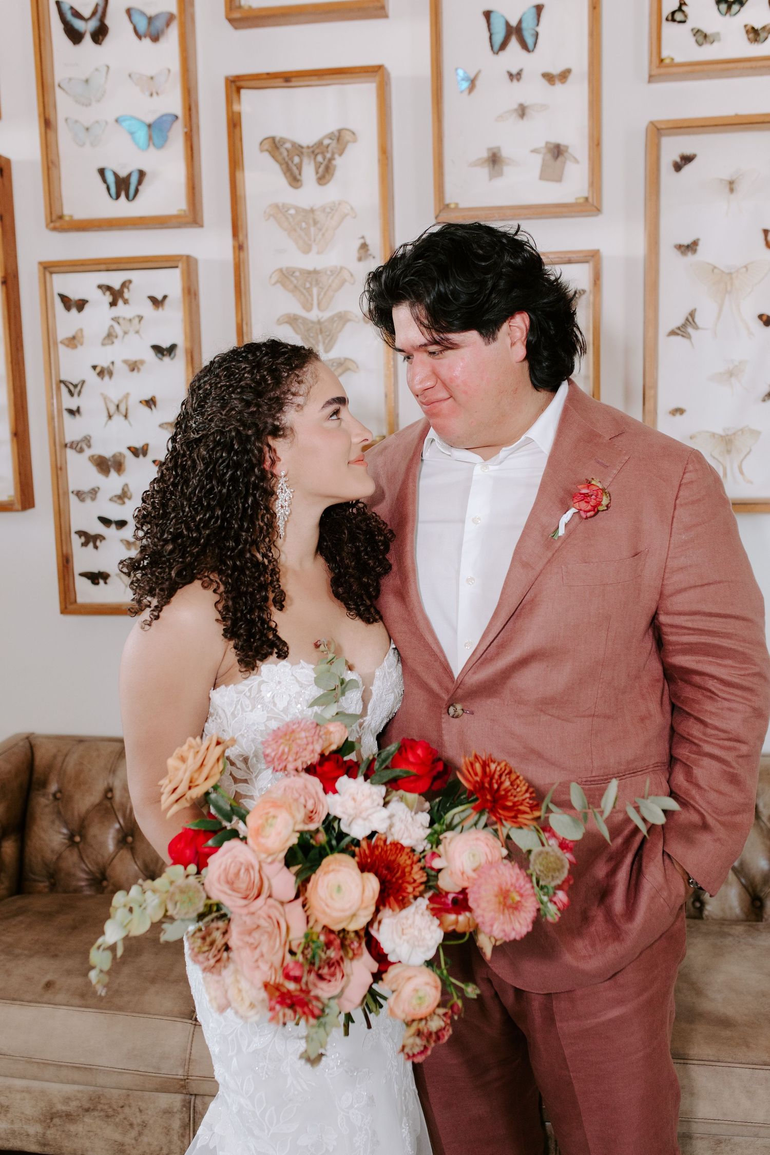 A romantic portrait against a wall of butterfly specimens with a pink and coral bouquet.