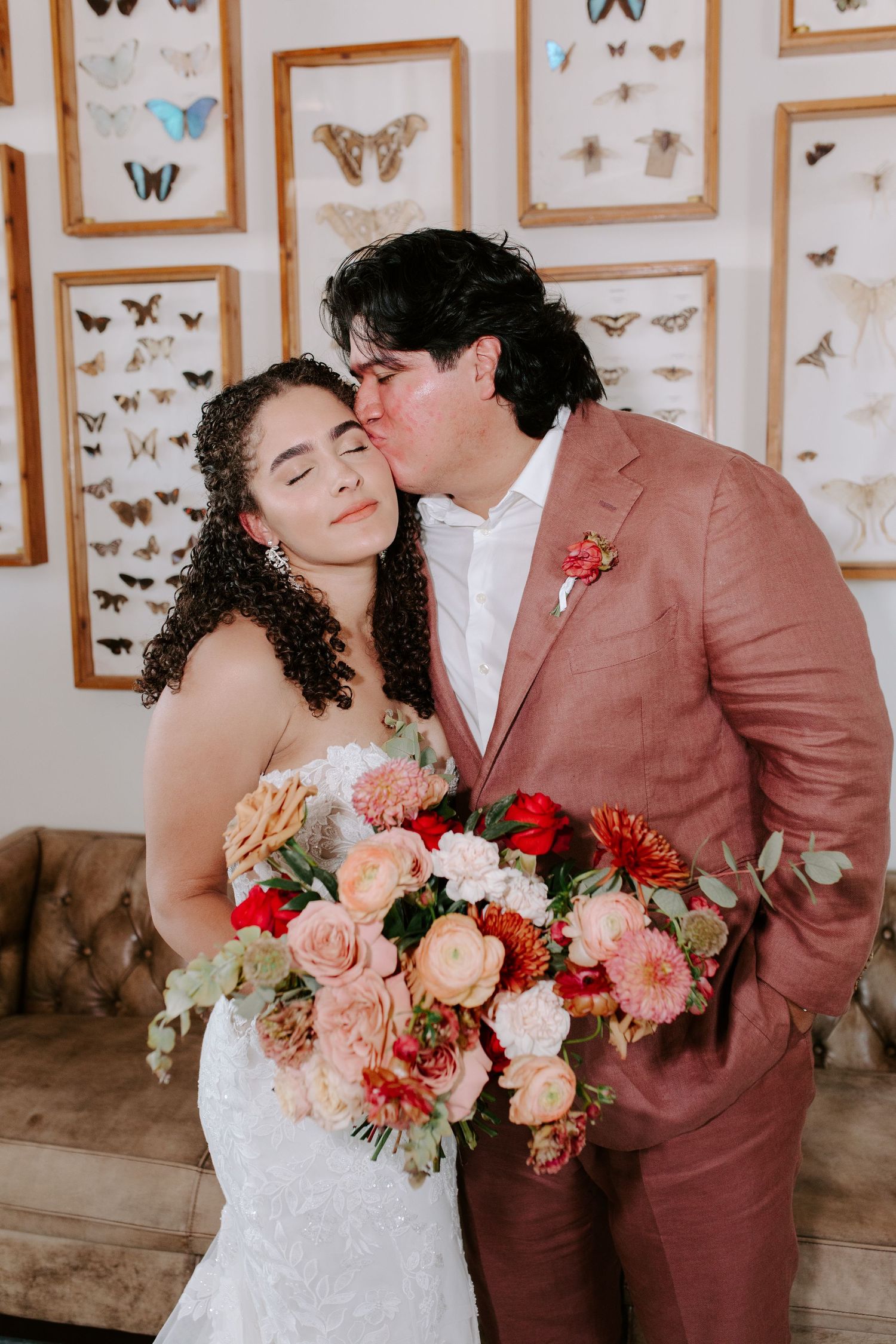An intimate wedding moment captured against a backdrop of framed butterfly collections.