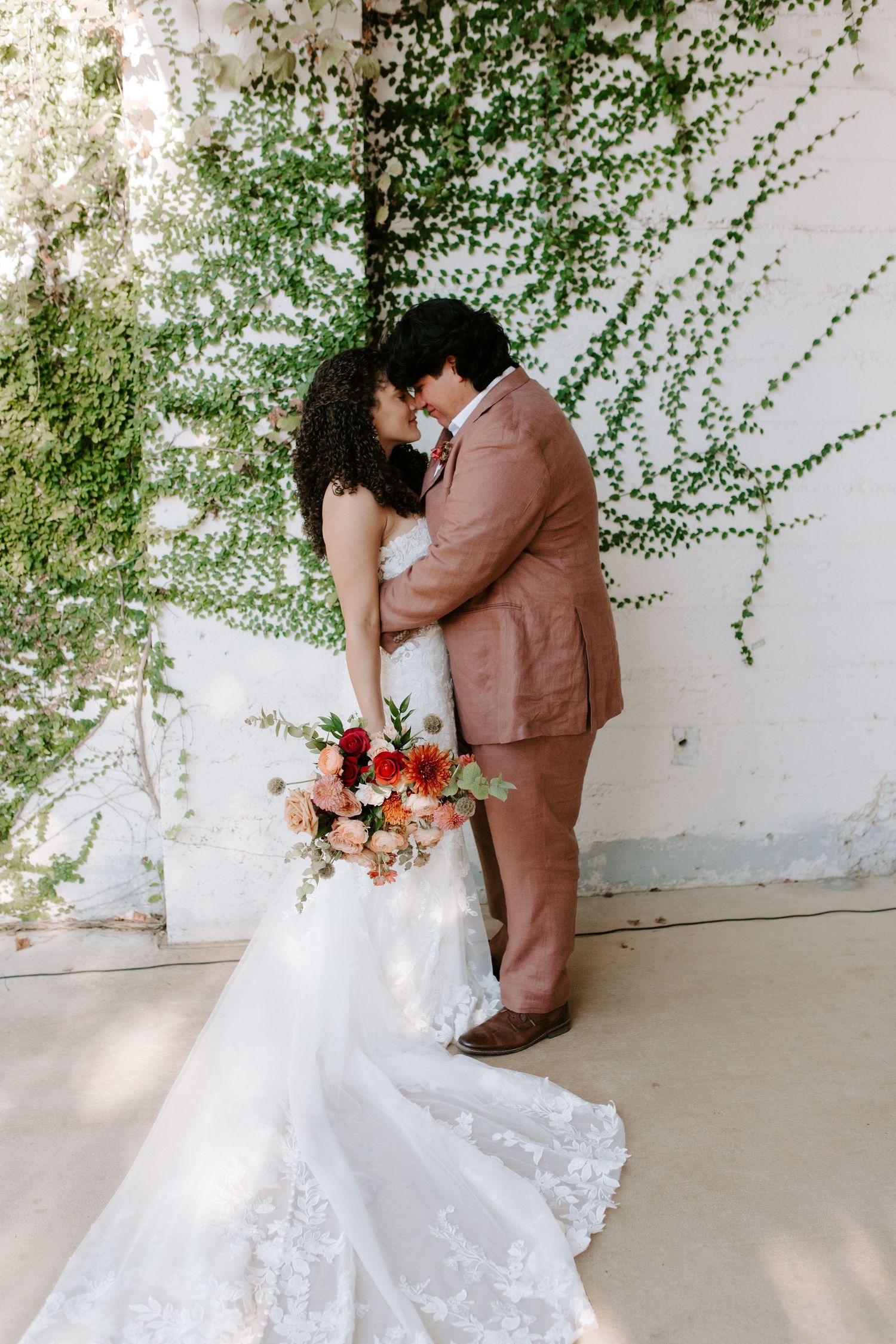 Romantic wedding portrait with couple embracing against a vine-covered wall.