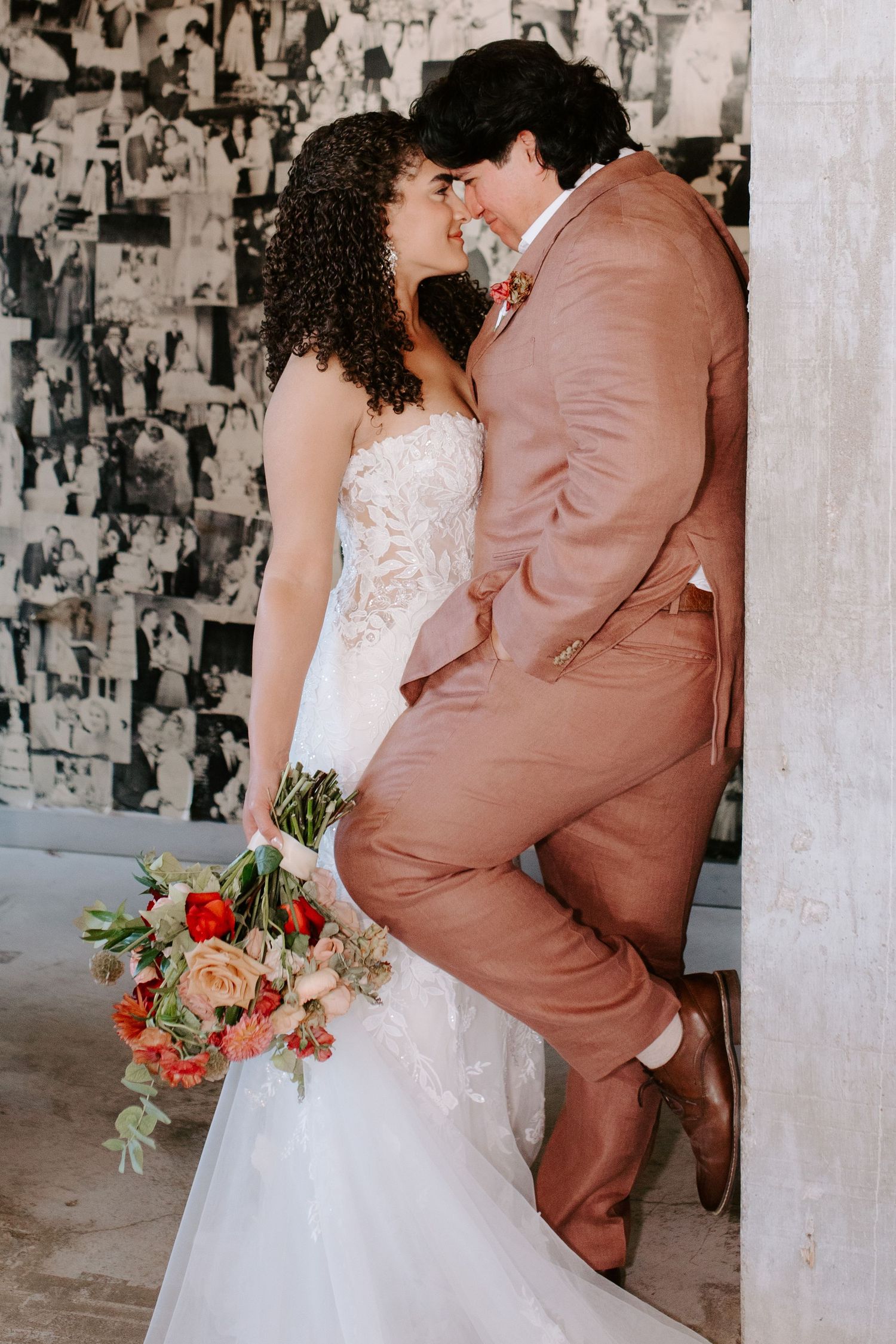 Intimate wedding portrait with couple in white dress and pink suit against textured wall.