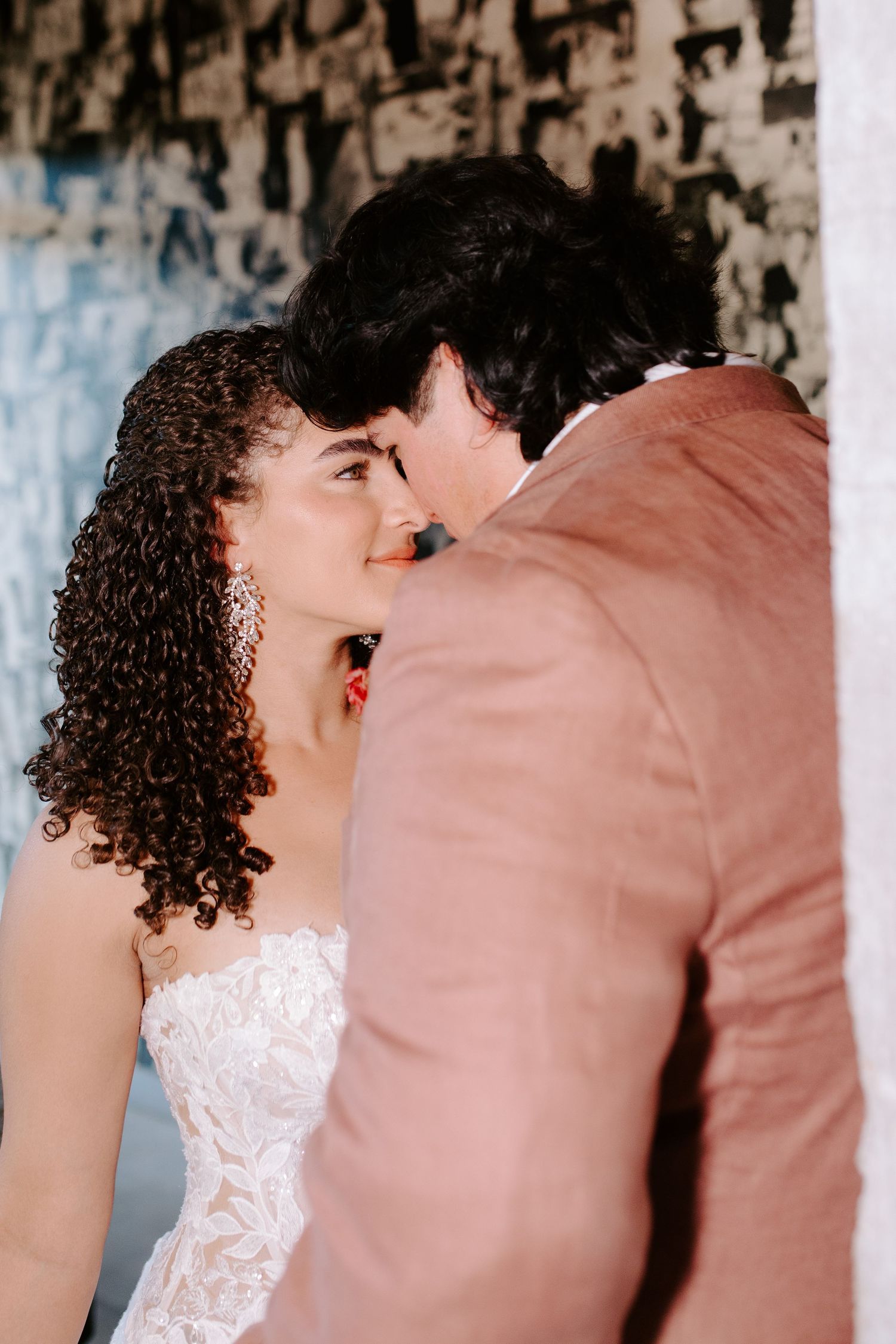 Close-up wedding photo showing tender moment between bride with curly hair and groom in pink suit.