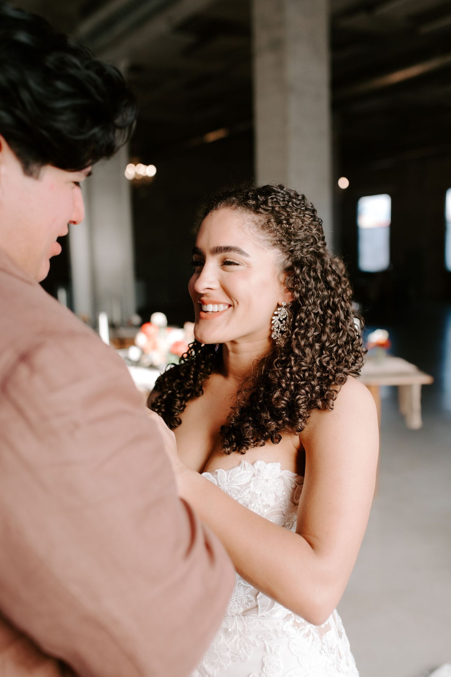 Joyful wedding couple shares intimate dance moment in industrial venue with twinkling lights.