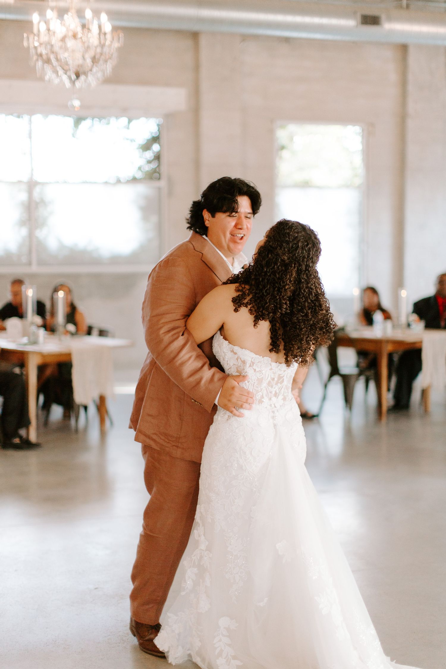 Couple shares romantic dance moment in light-filled reception venue with chandelier.
