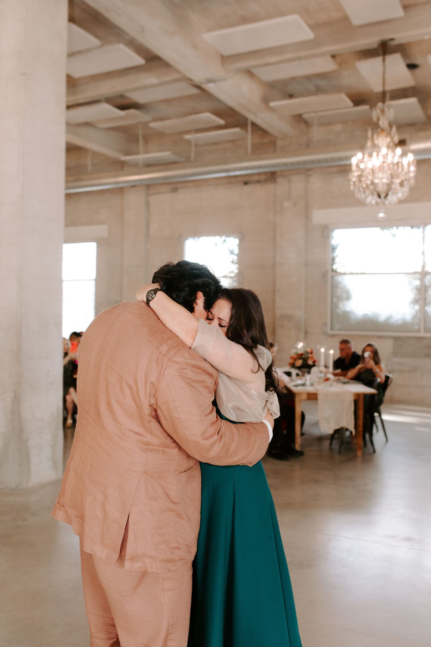 A couple embraces while dancing in an elegant reception venue with chandeliers.