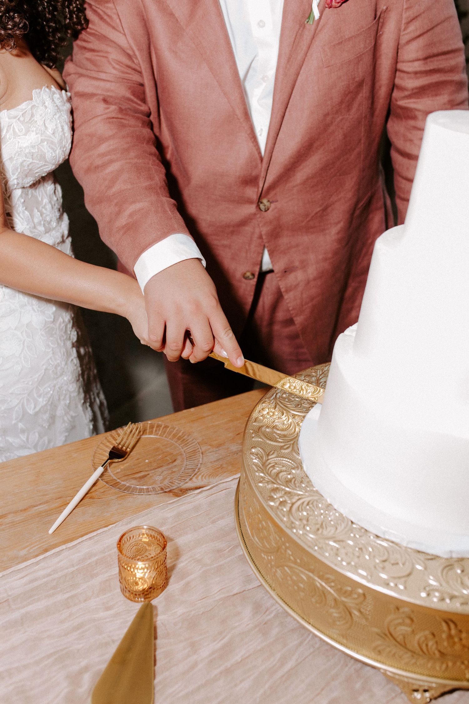 Close-up of hands cutting a white wedding cake on an ornate gold cake stand.