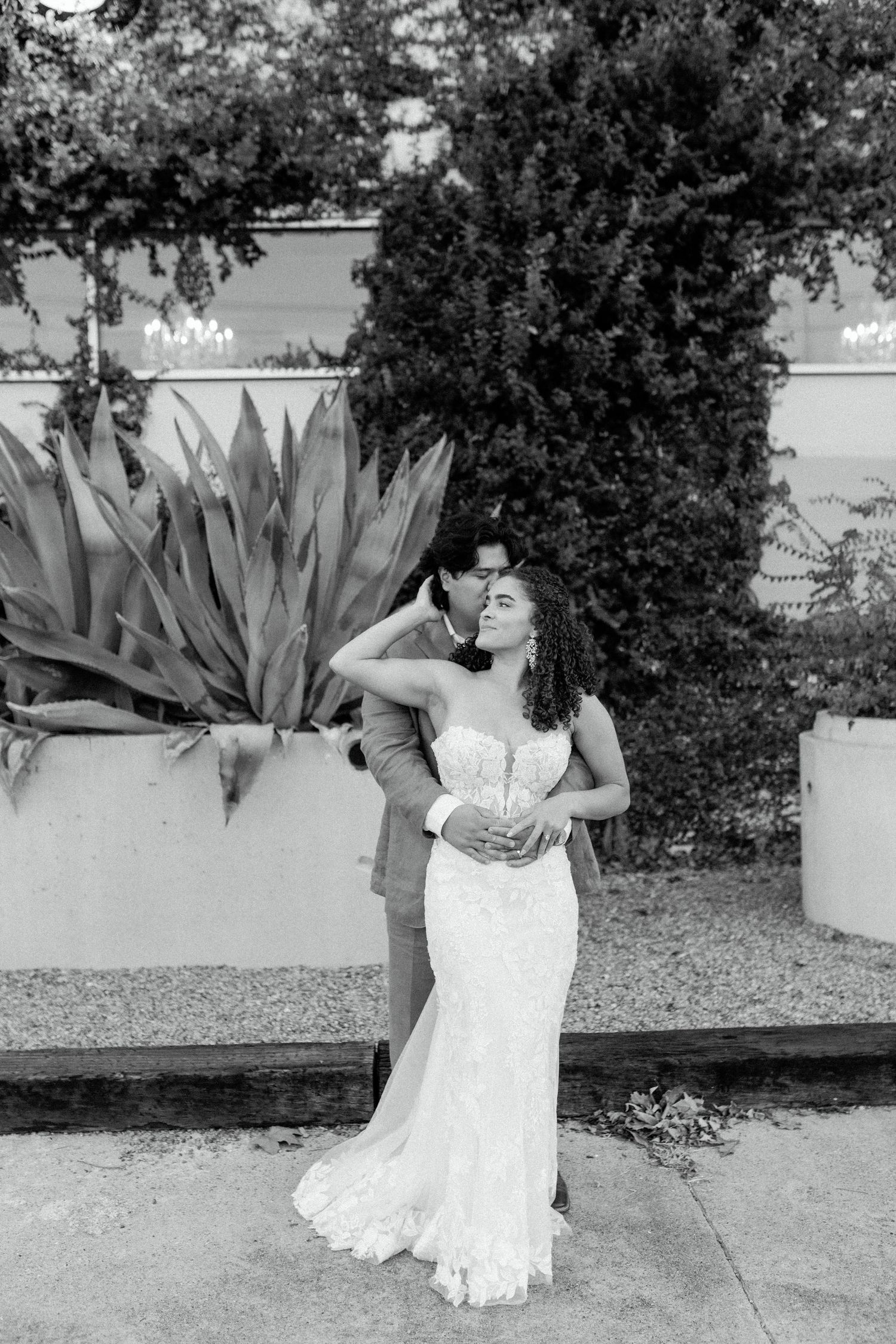 A romantic black and white portrait of a couple embracing by agave plants.