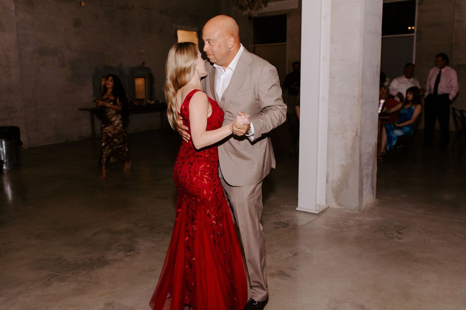 Couple dances at wedding reception with person in red gown and light colored suit.