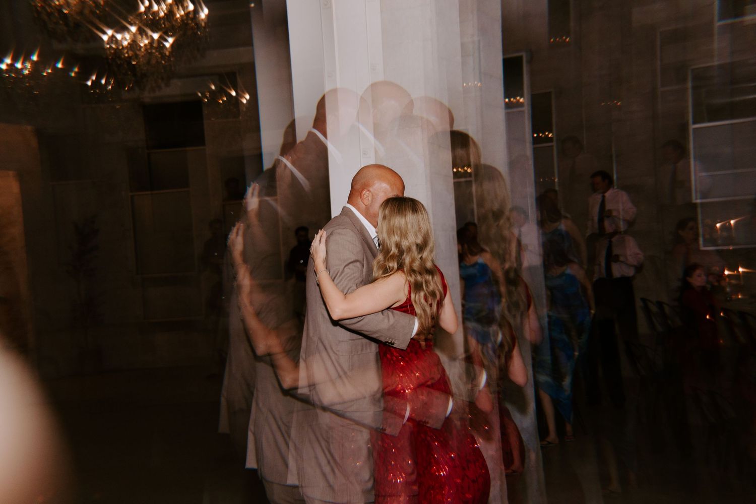 Wedding dance captured in warm lighting with couple in red gown and beige suit.
