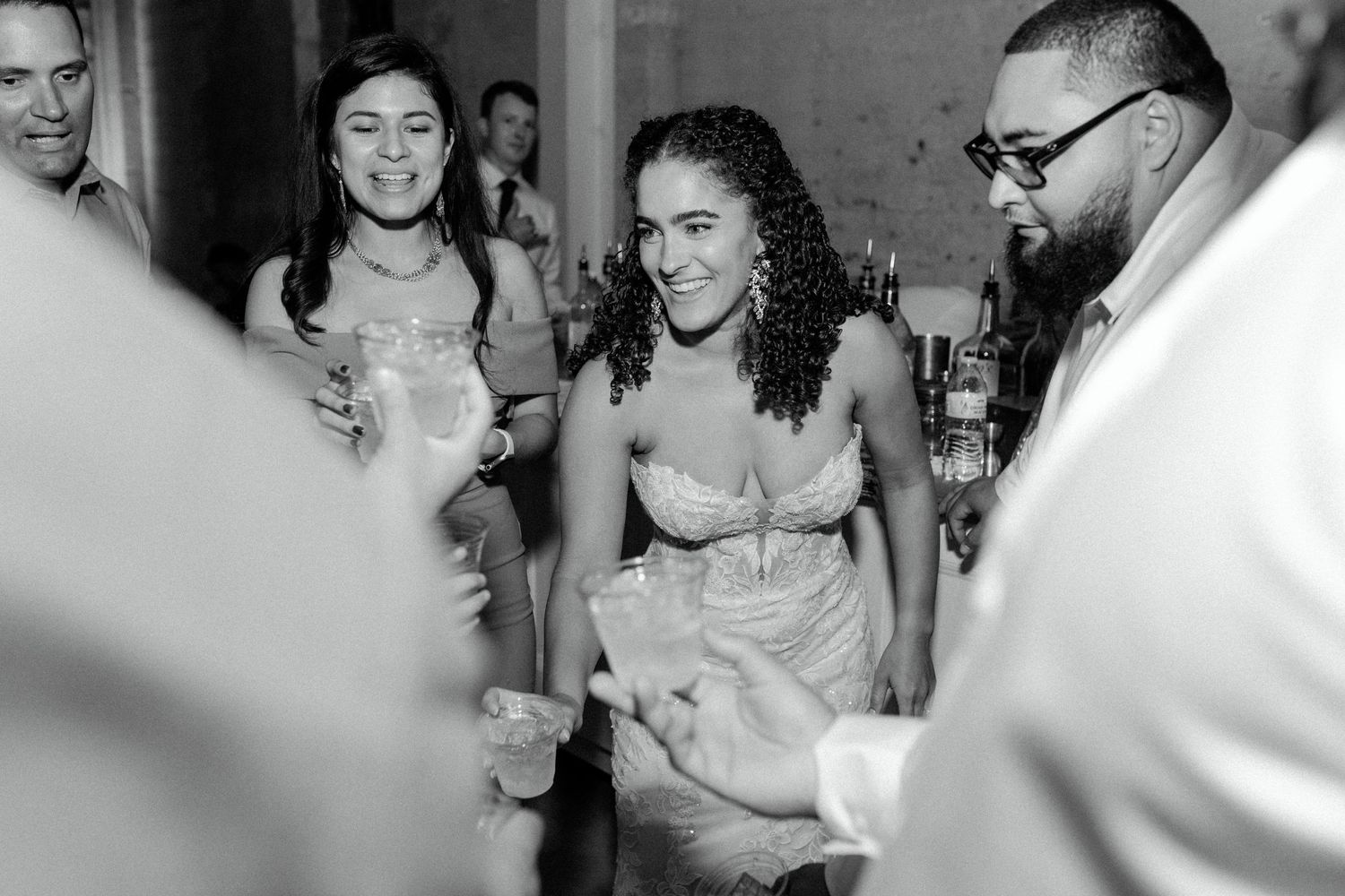 Wedding guests gather around for drinks and celebration at an indoor reception.