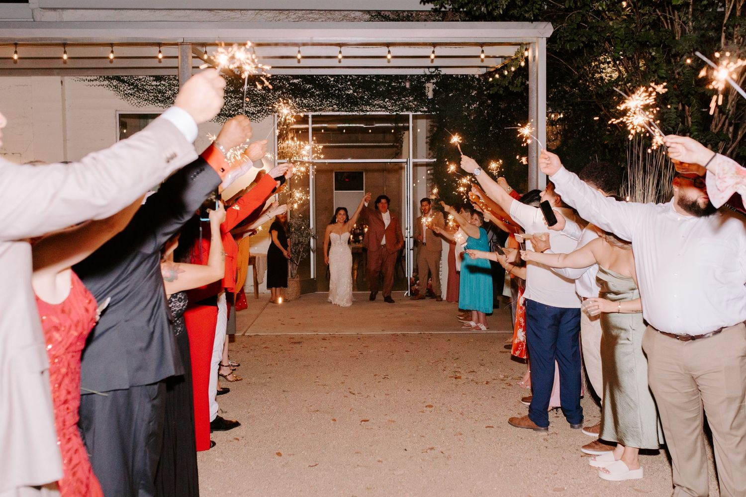 Wedding guests hold sparklers forming an illuminated exit pathway for the newlyweds.
