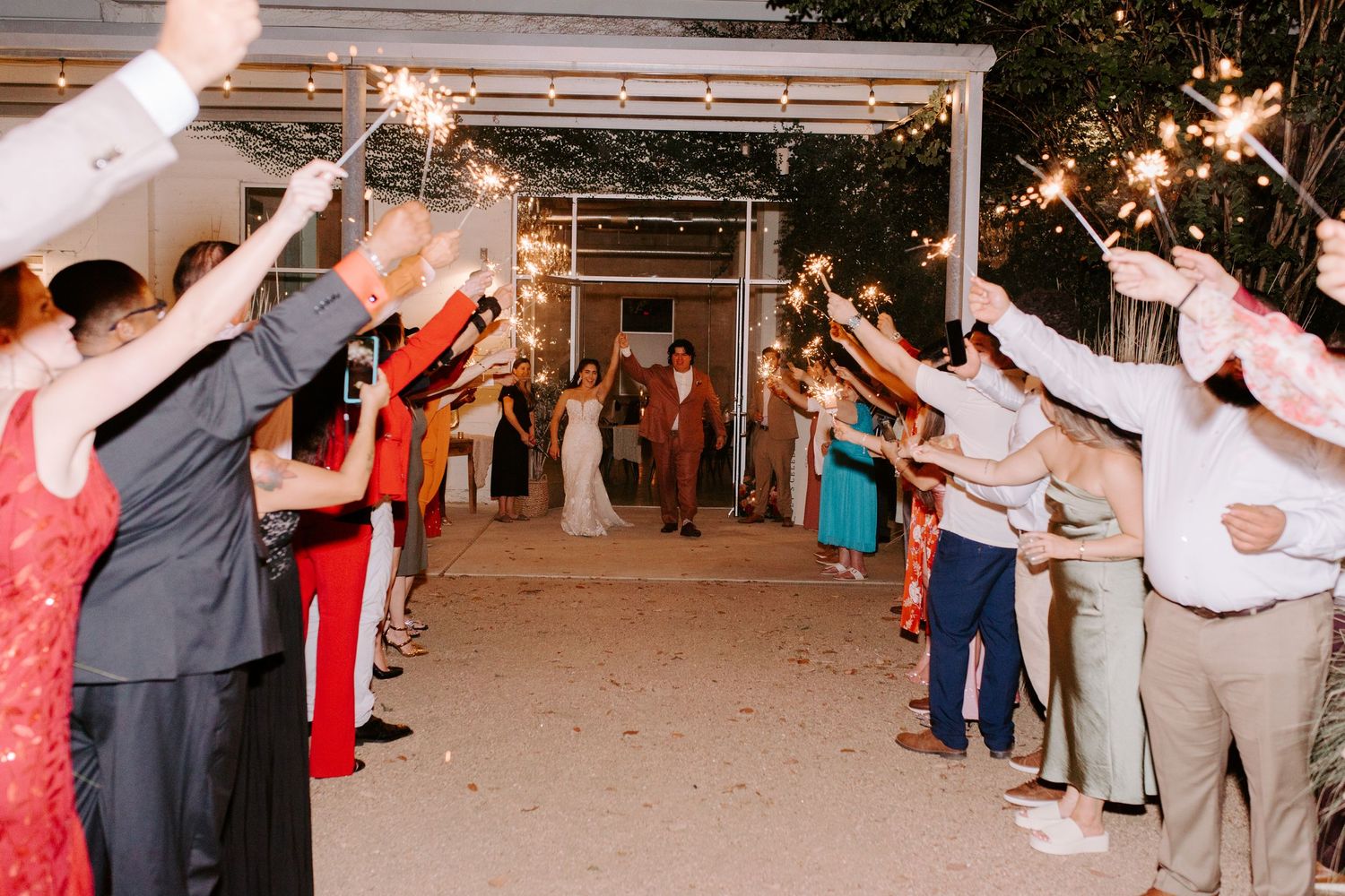Guests line up with sparklers creating a grand exit tunnel at an outdoor wedding venue.