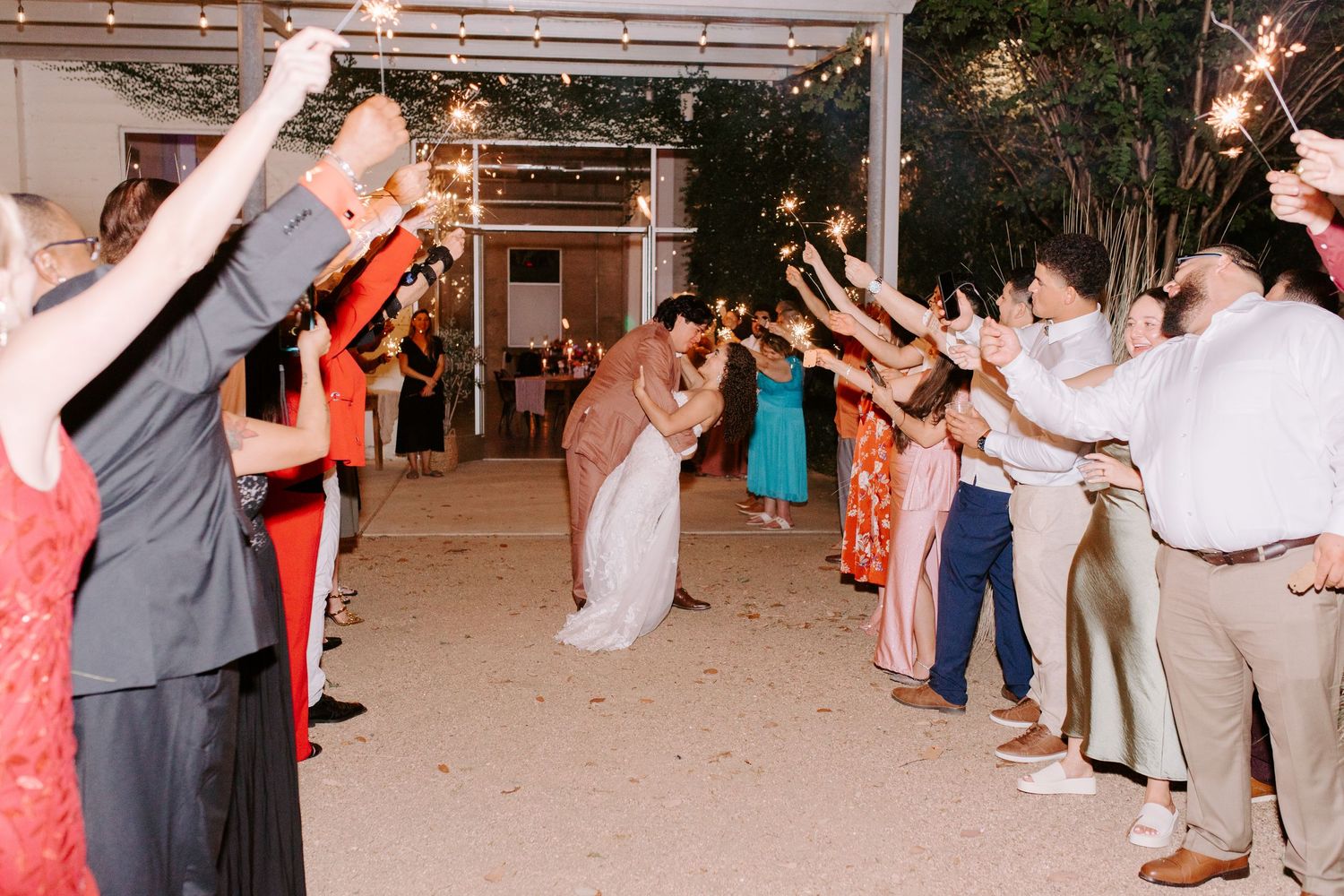 Newlyweds walk through a sparkler exit tunnel lined with cheering wedding guests.