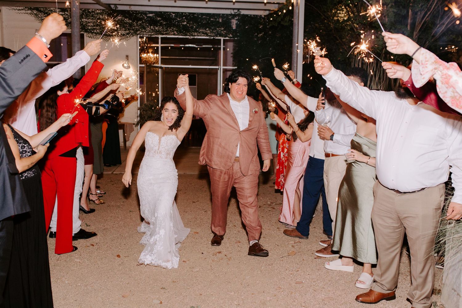 A wedding couple makes their grand exit through a sparkler-lit path surrounded by guests.