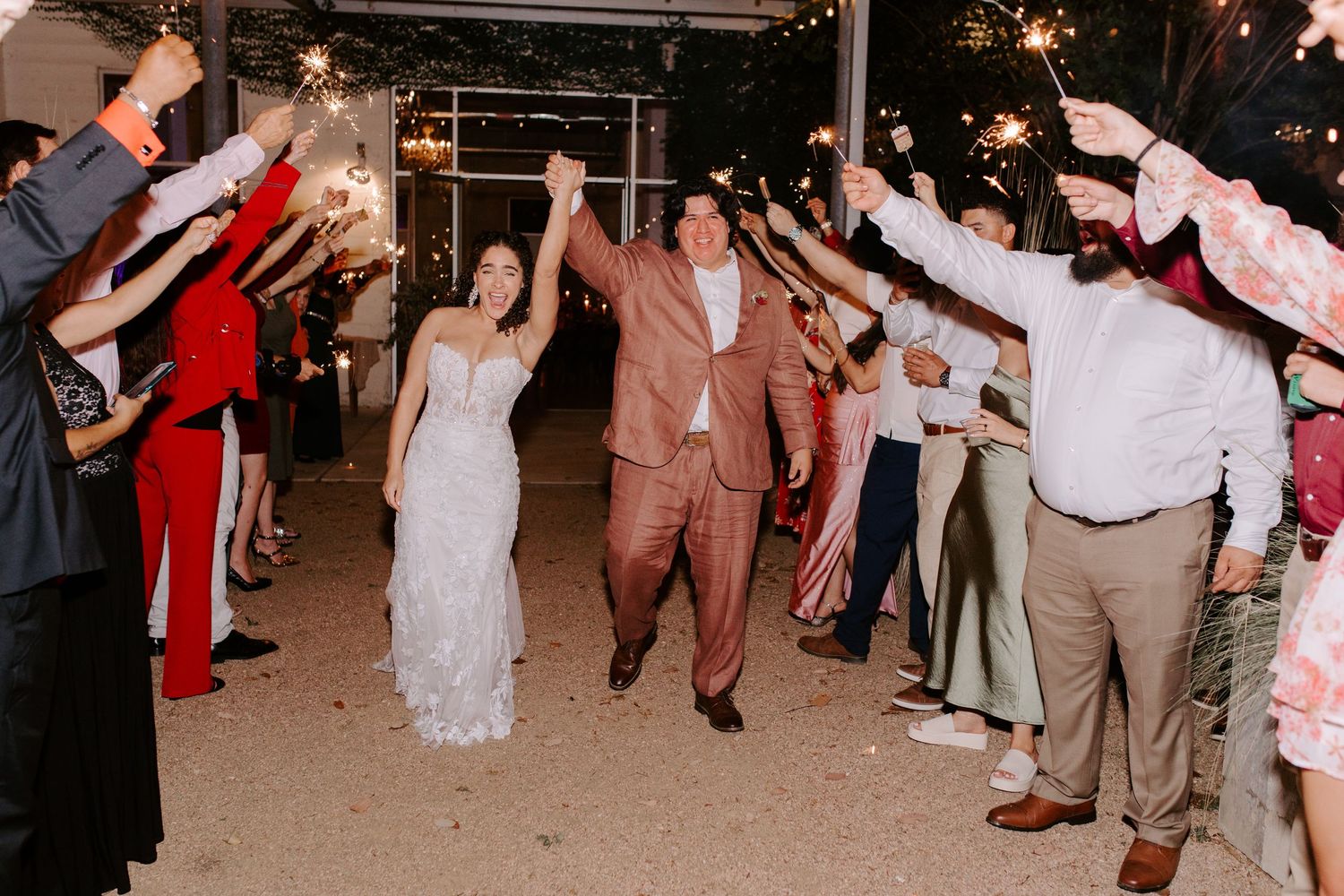 Bride and groom celebrate while walking through a sparkler tunnel at their wedding exit.