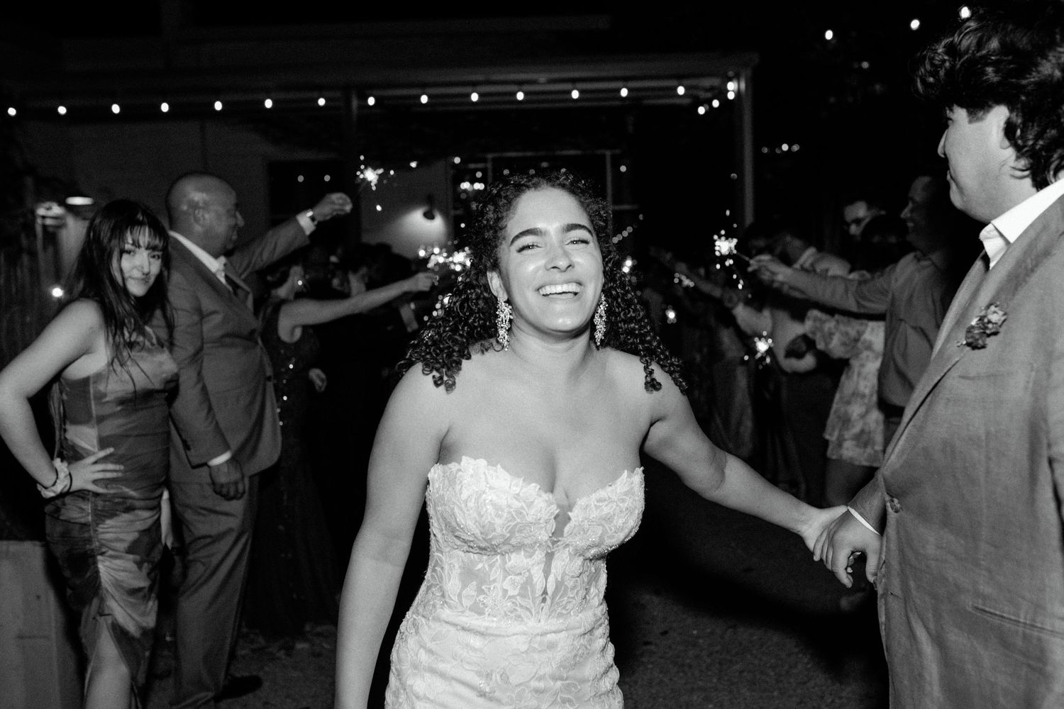 Wedding guests dance joyfully at reception under string lights.