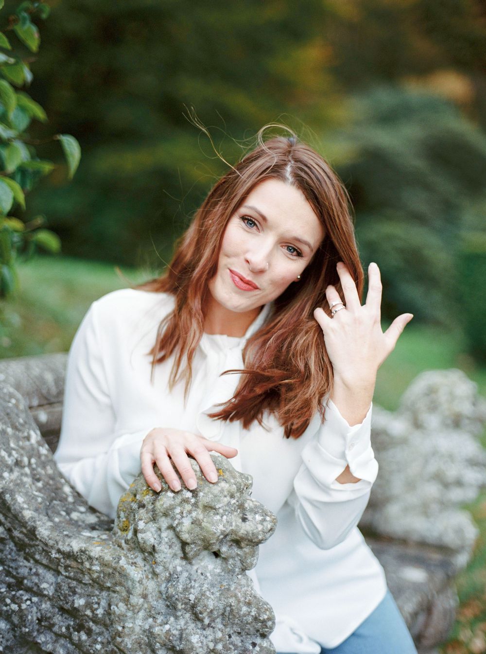 Person in a white sweater sitting on rock formations in a natural outdoor setting with greenery in background.