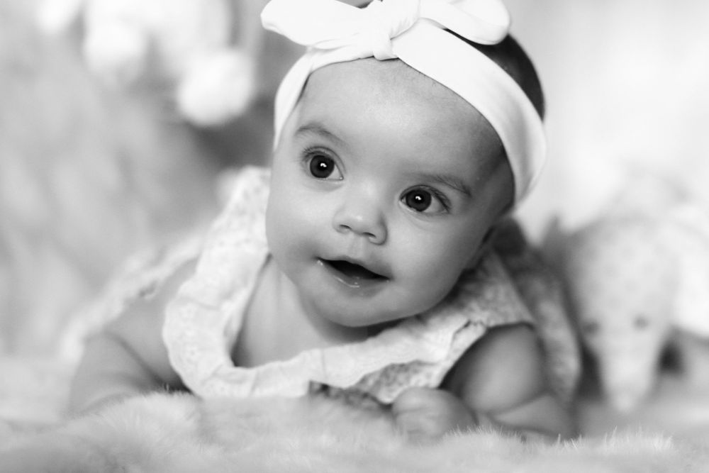 Sweet baby with bright eyes smiles while lying down in black and white photo series.