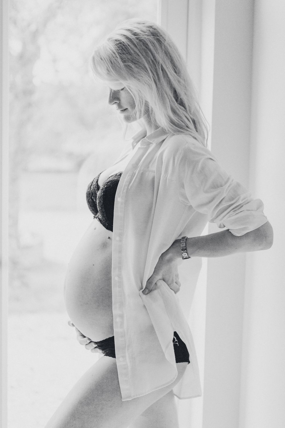 Maternity picture posing against bright window in elegant monochromatic series.