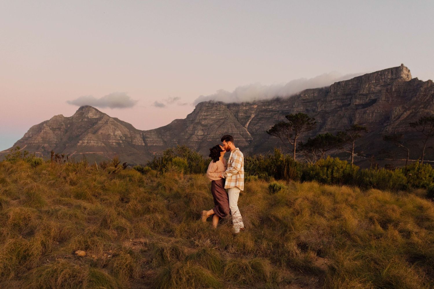 A couple shares an intimate moment at sunset on Signal Hill with views of Table Mountain in the background.