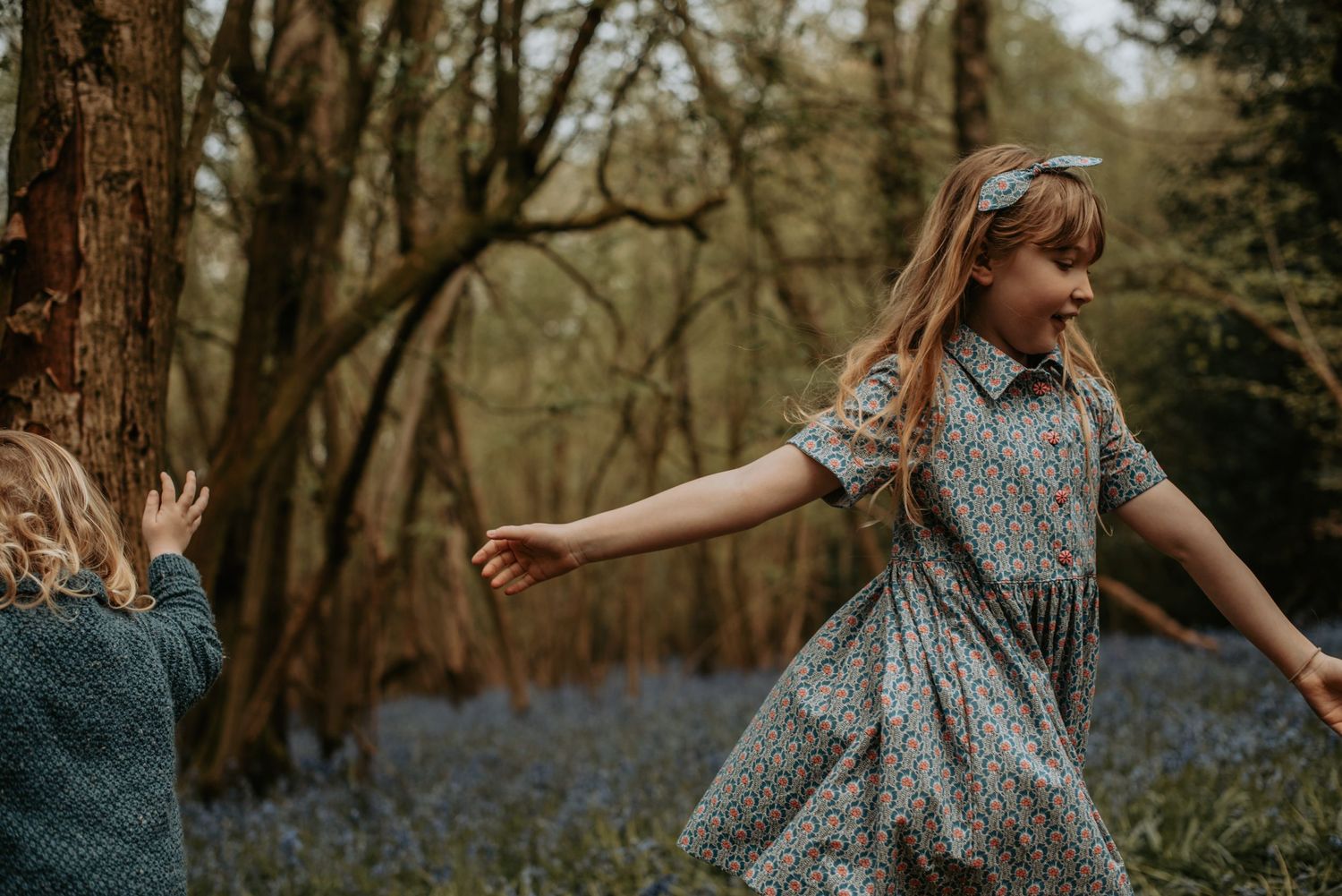 Two children play joyfully in a spring forest filled with blooming bluebells and golden sunlight.