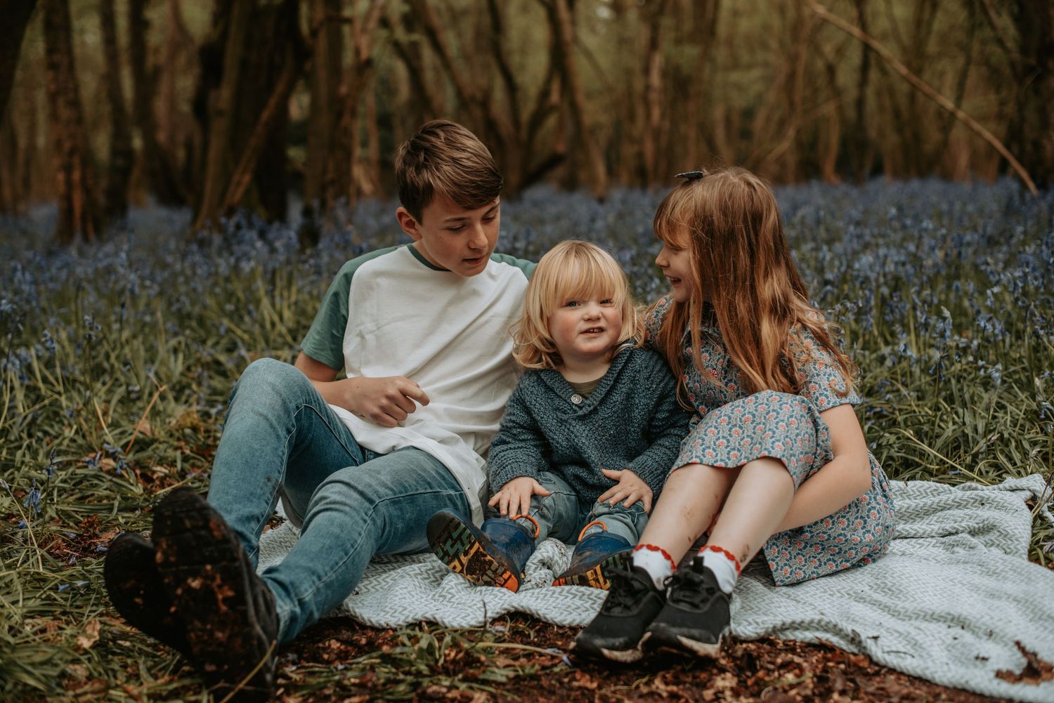 Family sitting together on blanket in spring forest surrounded by blooming bluebells.