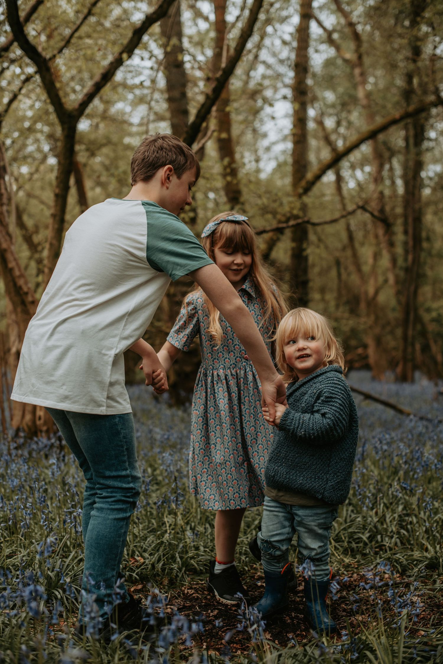 A family spends time together in a wooded area with bluebells blooming on the forest floor.