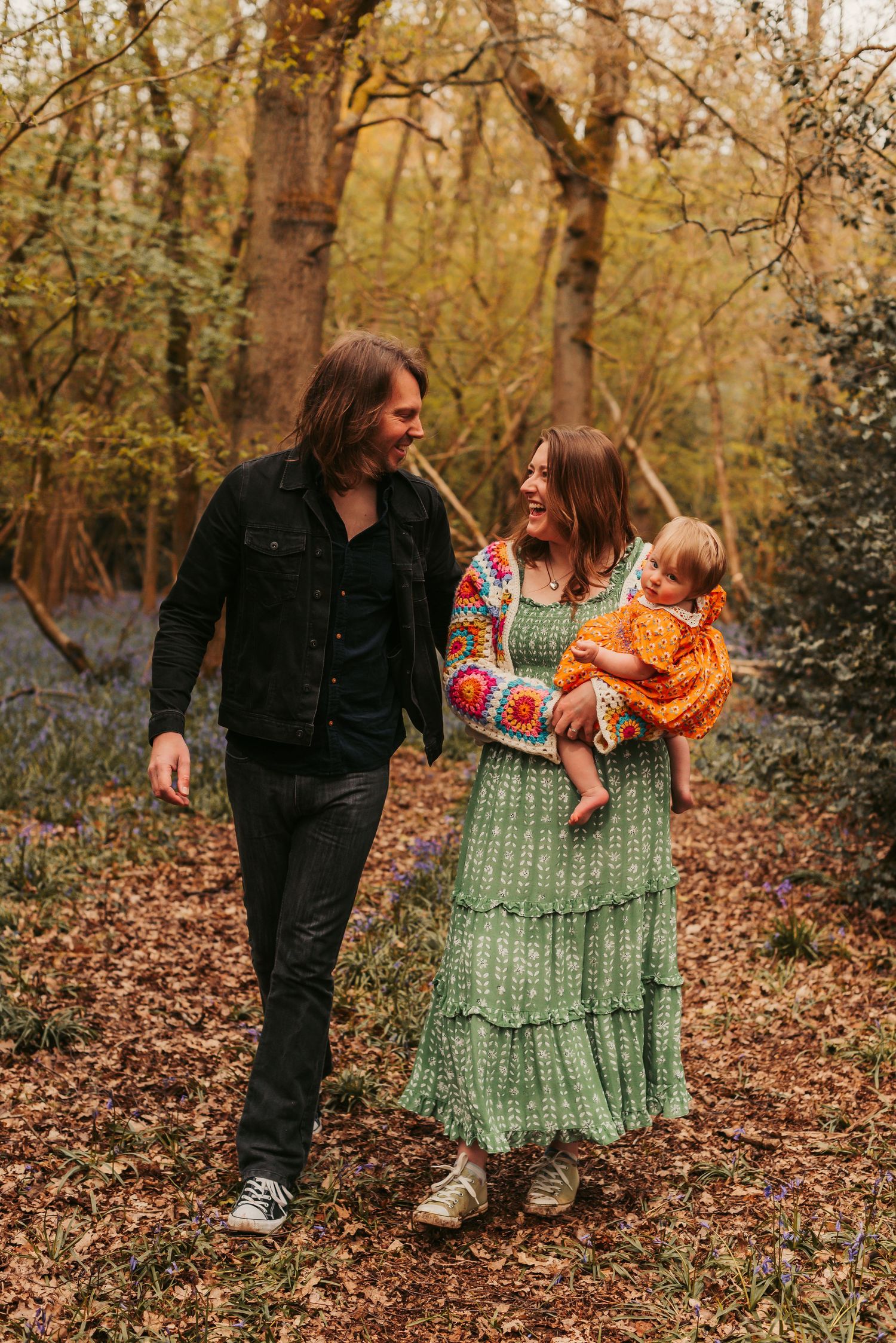 A family walks together through an autumn forest with fallen leaves, wearing casual attire and bohemian style clothing.