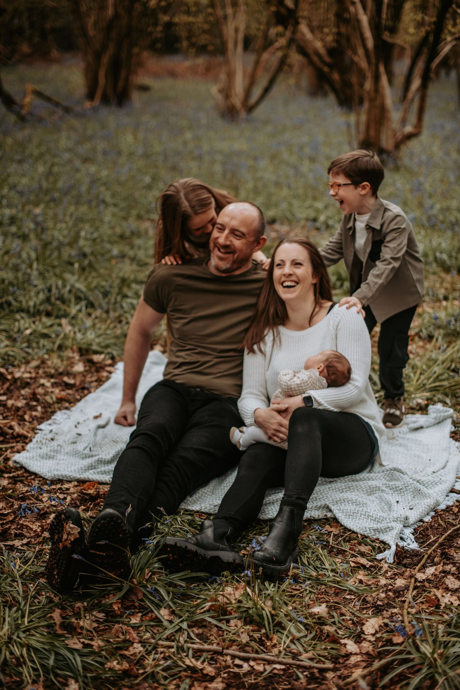Family enjoying a tender moment together while sitting on a white blanket in a wooded area during autumn.