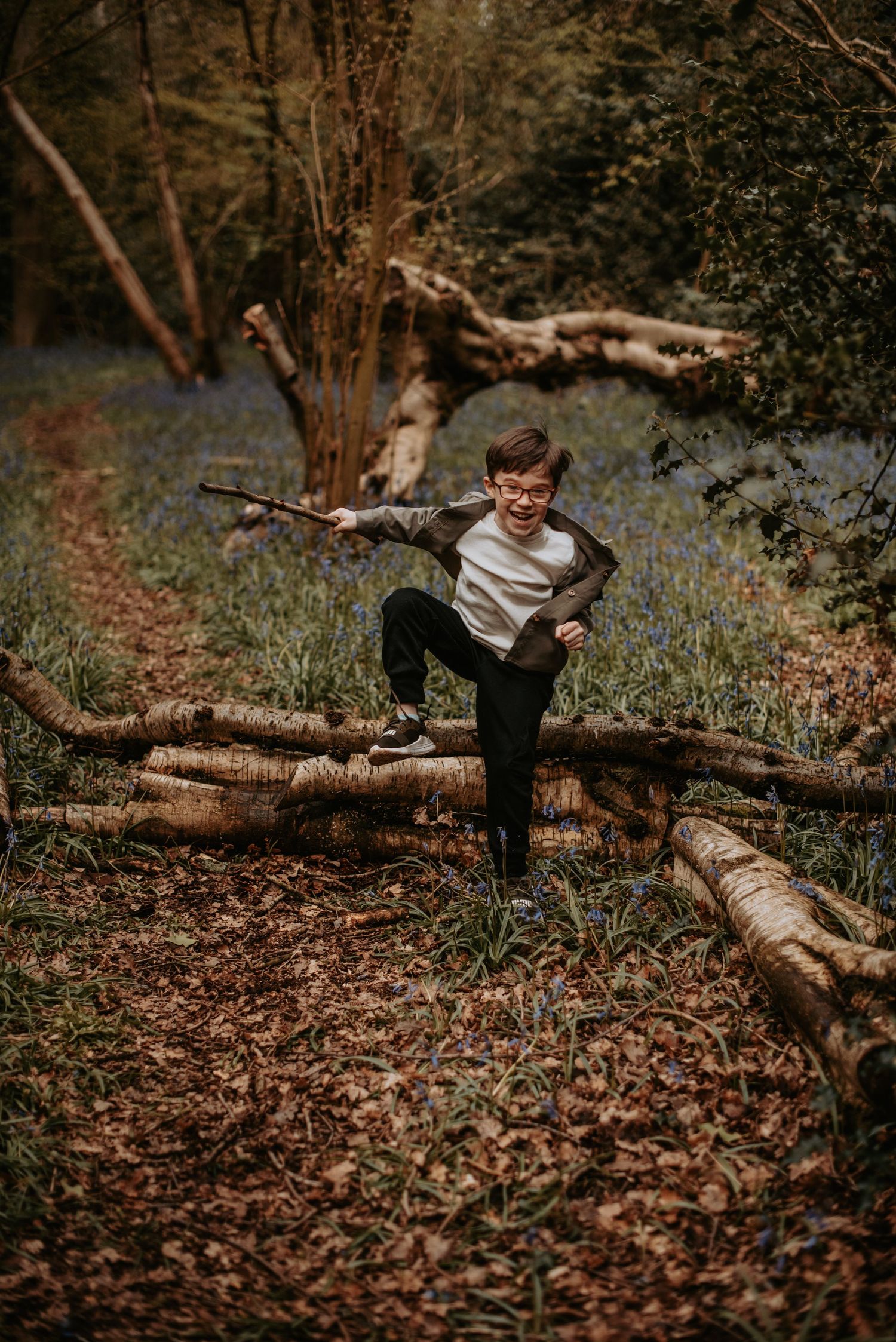 A child playfully balances on fallen logs in an autumn forest covered with brown leaves.