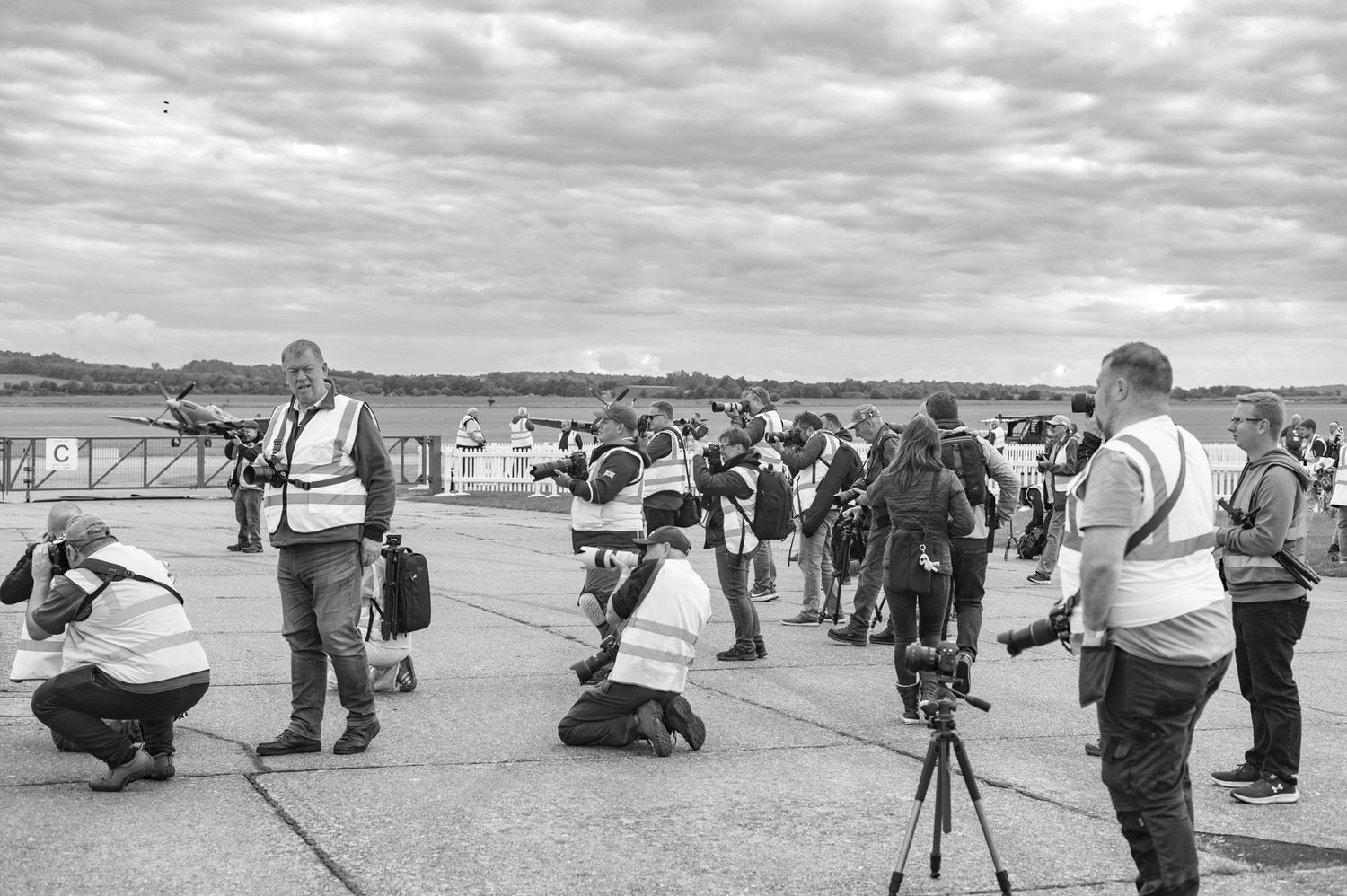 A group of photographers with cameras positioned on a flat outdoor viewing area under cloudy skies.