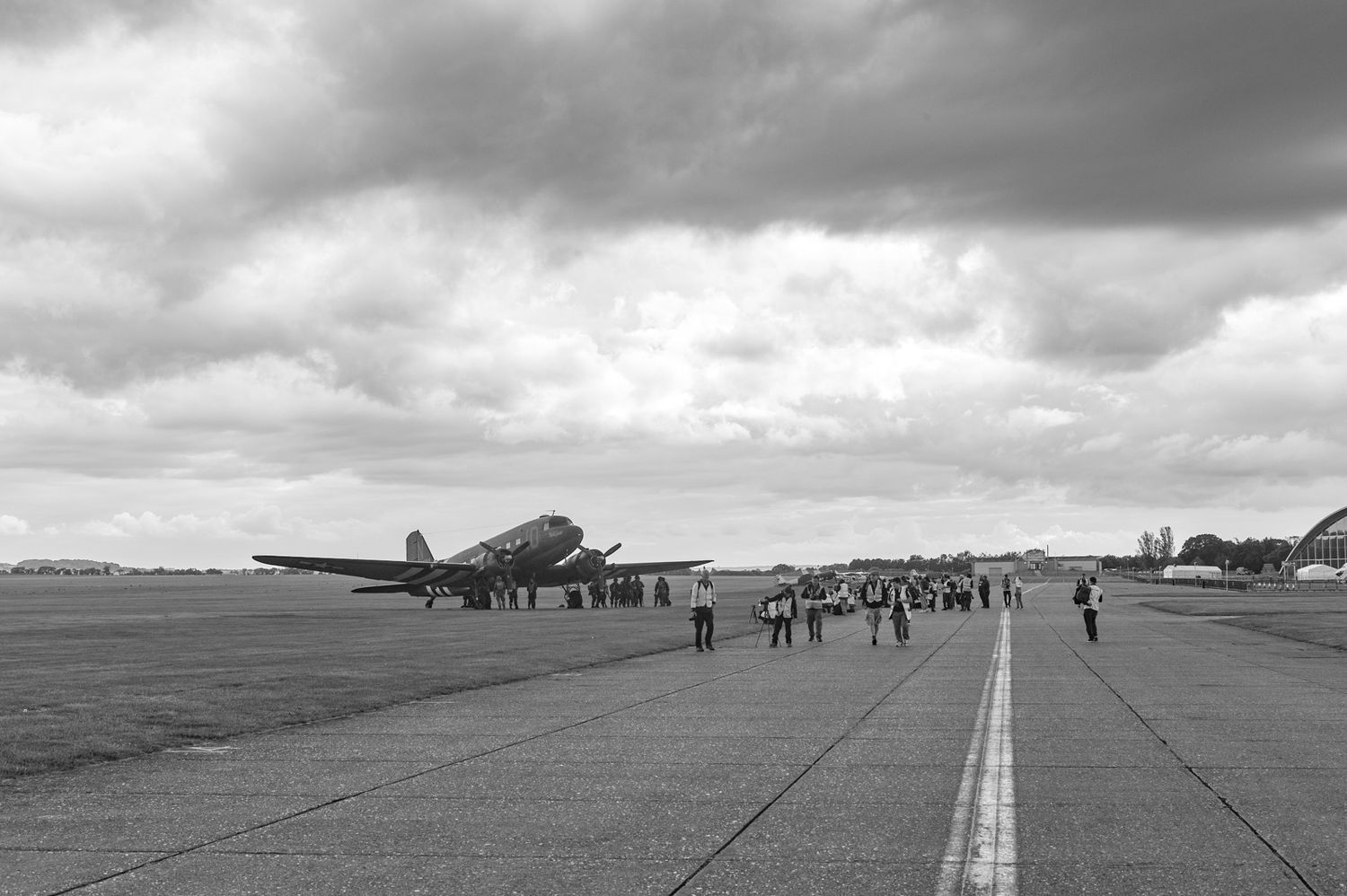 Vintage black and white image of aircraft parked on runway with people gathered on tarmac.