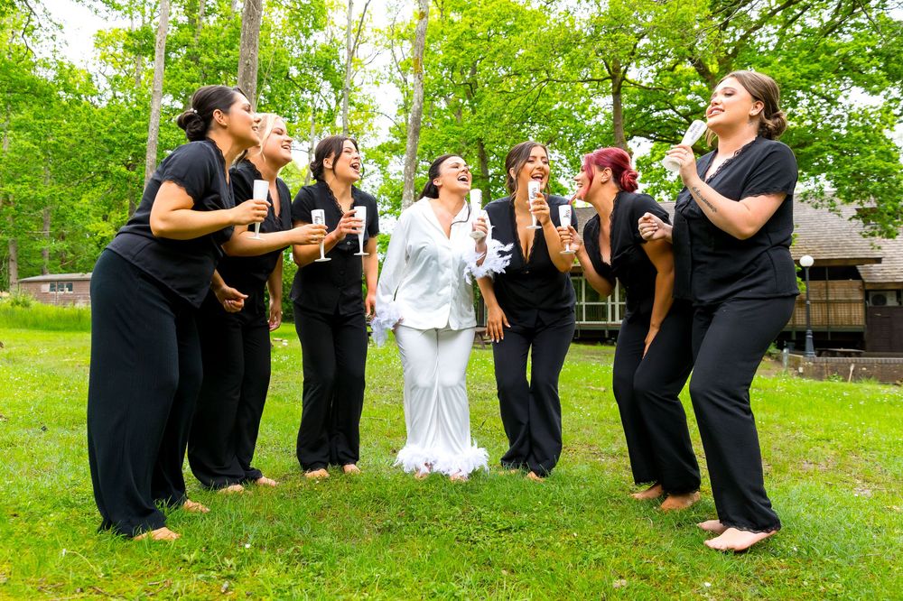 Bride and bridesmaids laughing together outdoors in matching pyjamas holding personalised champagne flutes.