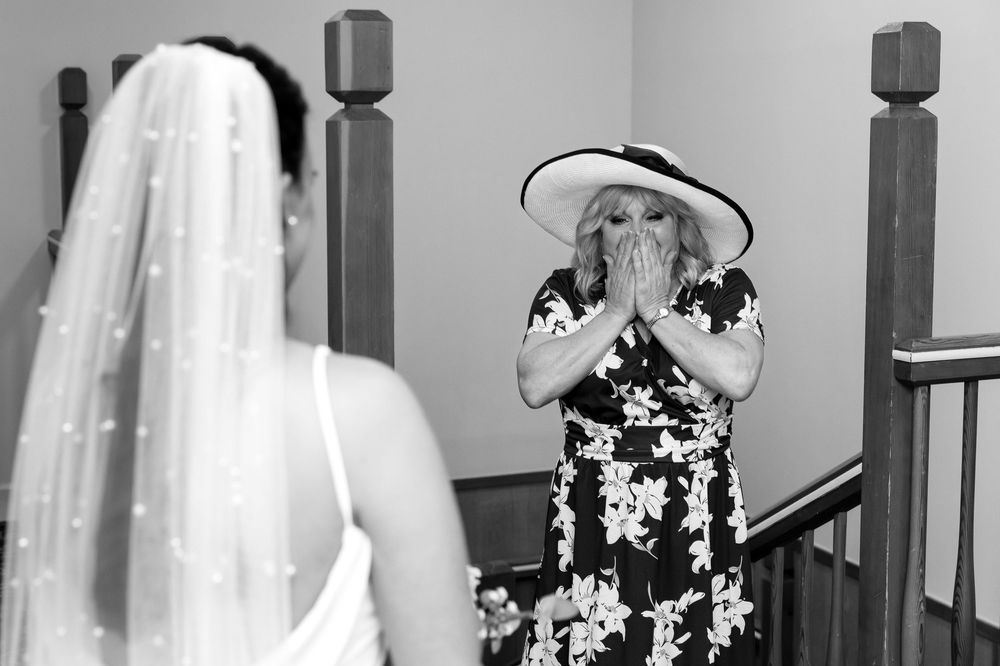 Emotional moment as mother sees the bride for the first time, hands over mouth in surprise.