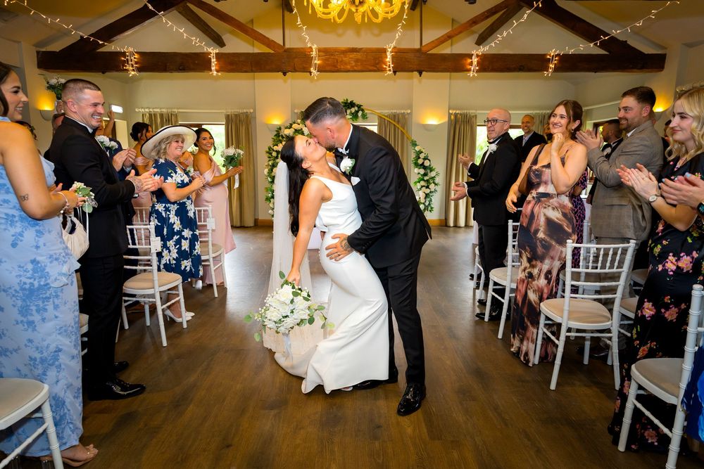 Bride and groom share a romantic dip kiss at the end of the ceremony as guests cheer around them.