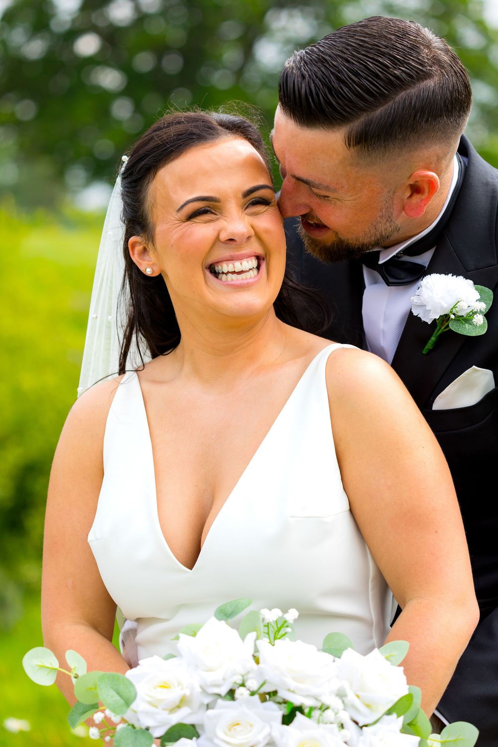 Bride laughing joyfully as the groom leans in close during their wedding portraits.