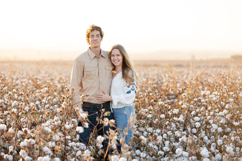A romantic couple poses together in a sun-lit cotton field during golden hour.