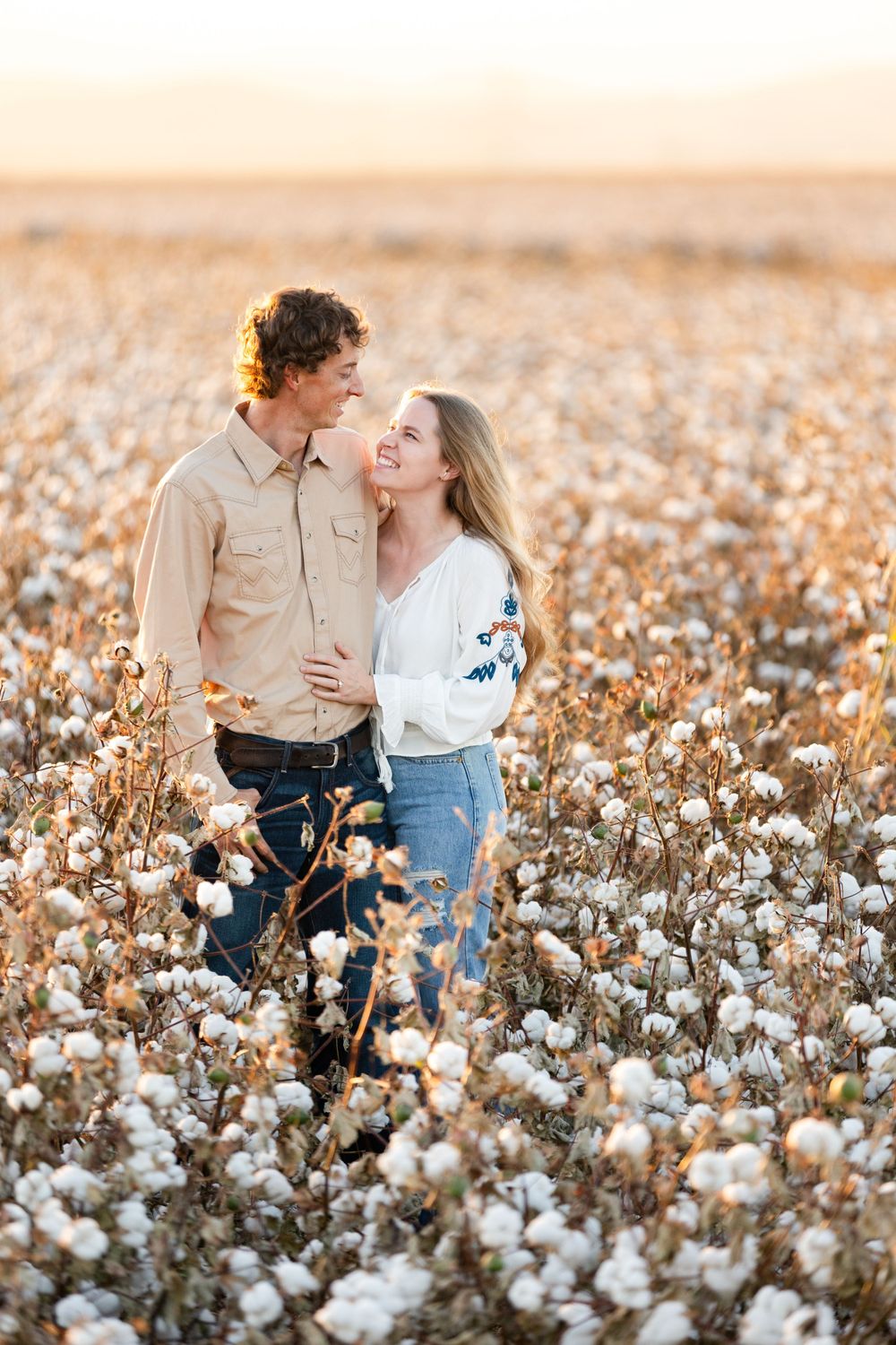 A romantic couple shares a tender moment while standing in a sunlit cotton field at golden hour.