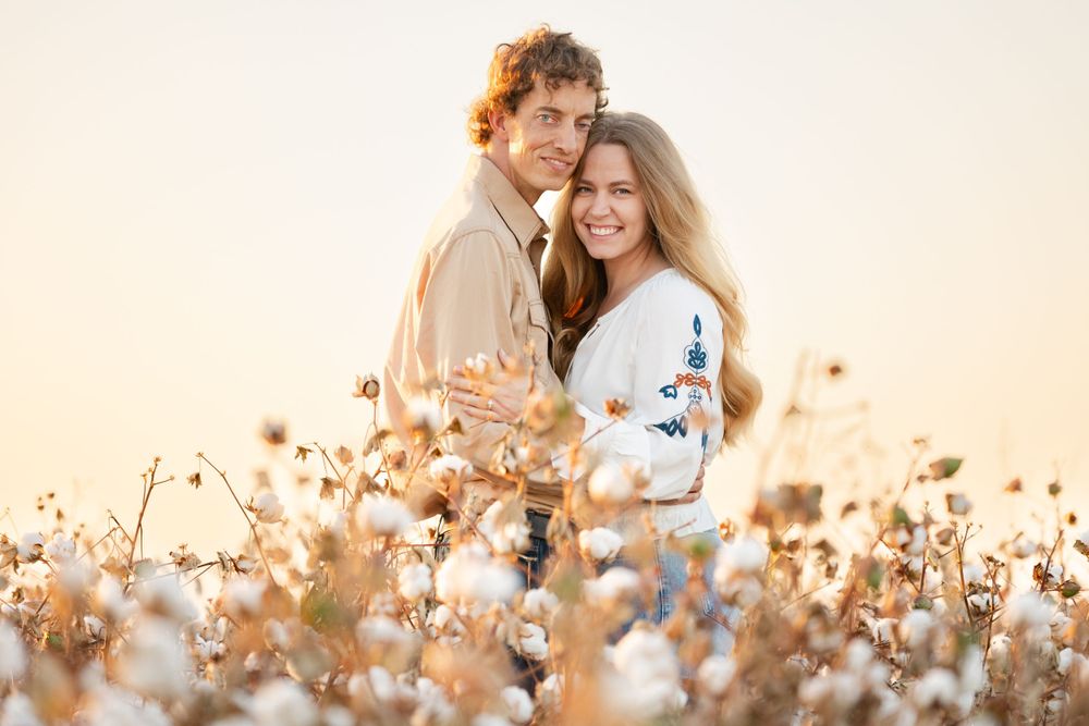 A couple shares an intimate embrace while standing in a glowing cotton field at dusk.
