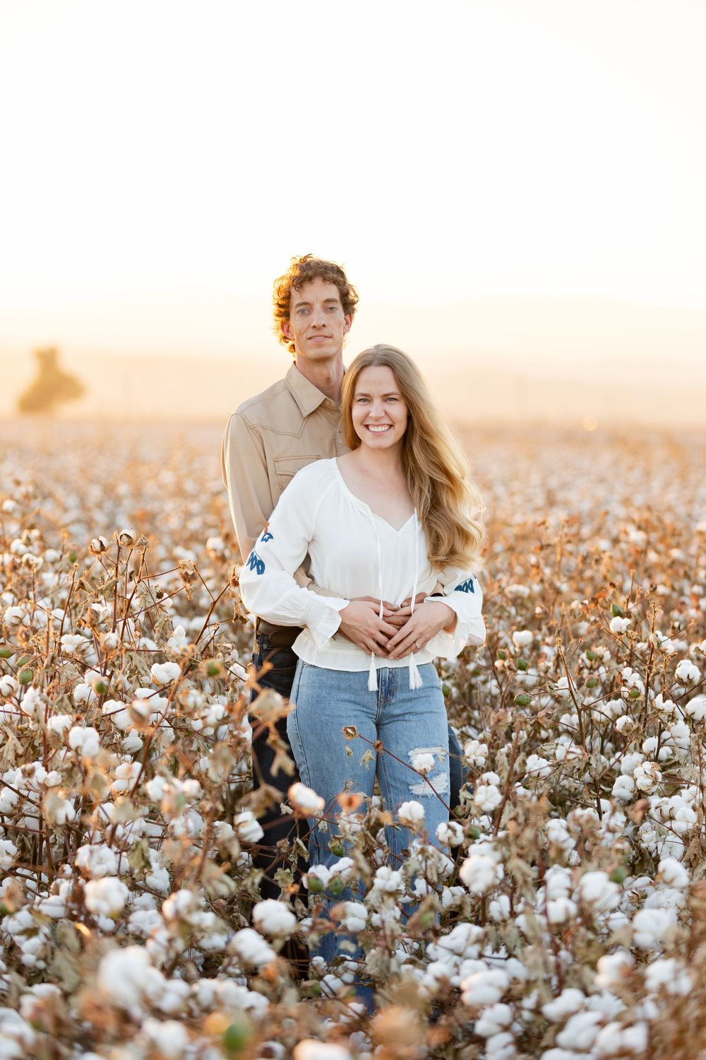 A couple poses together in a blooming cotton field at sunset.