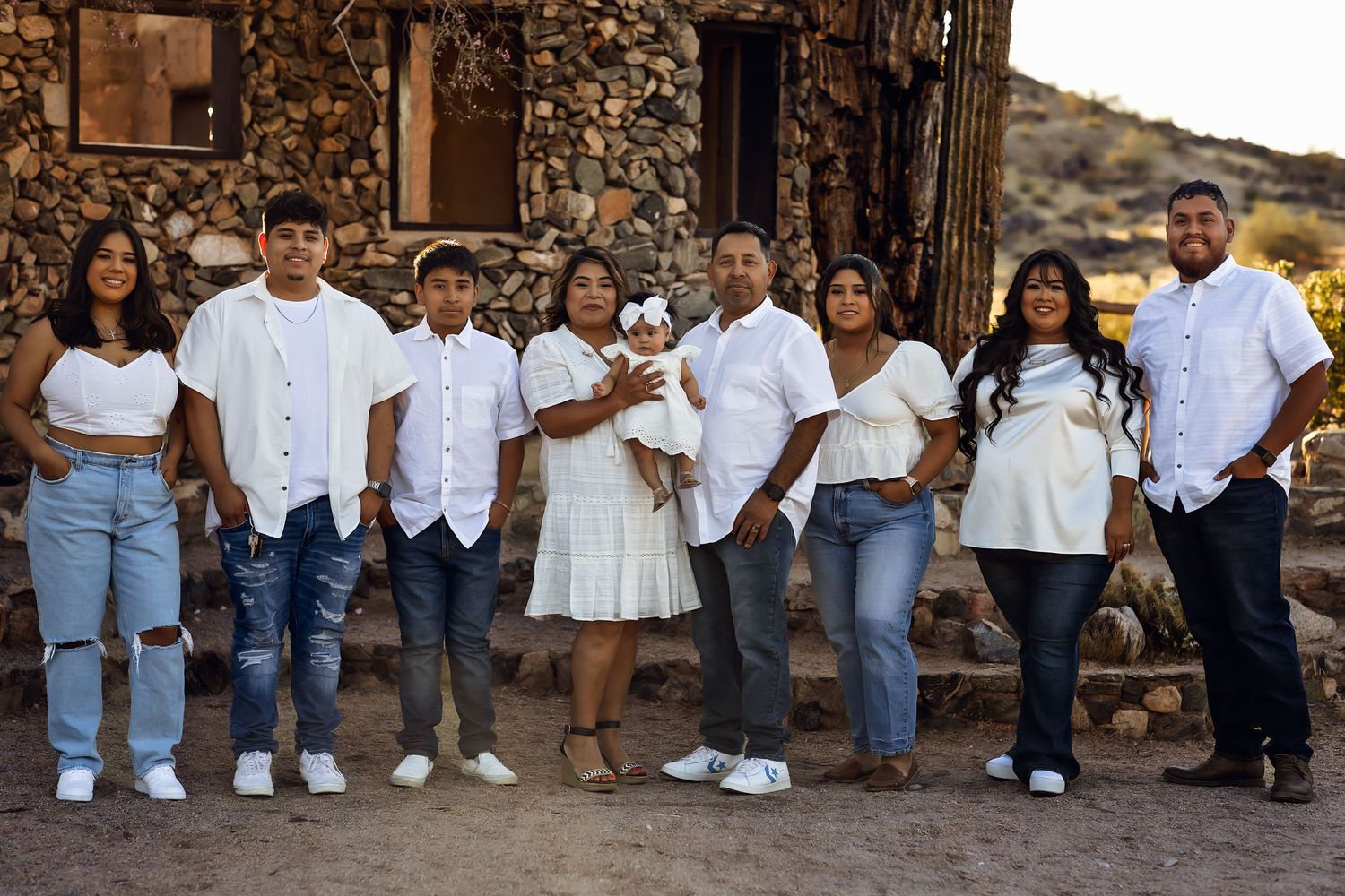 A family group poses outdoors against a stone wall wearing coordinated white and denim outfits.