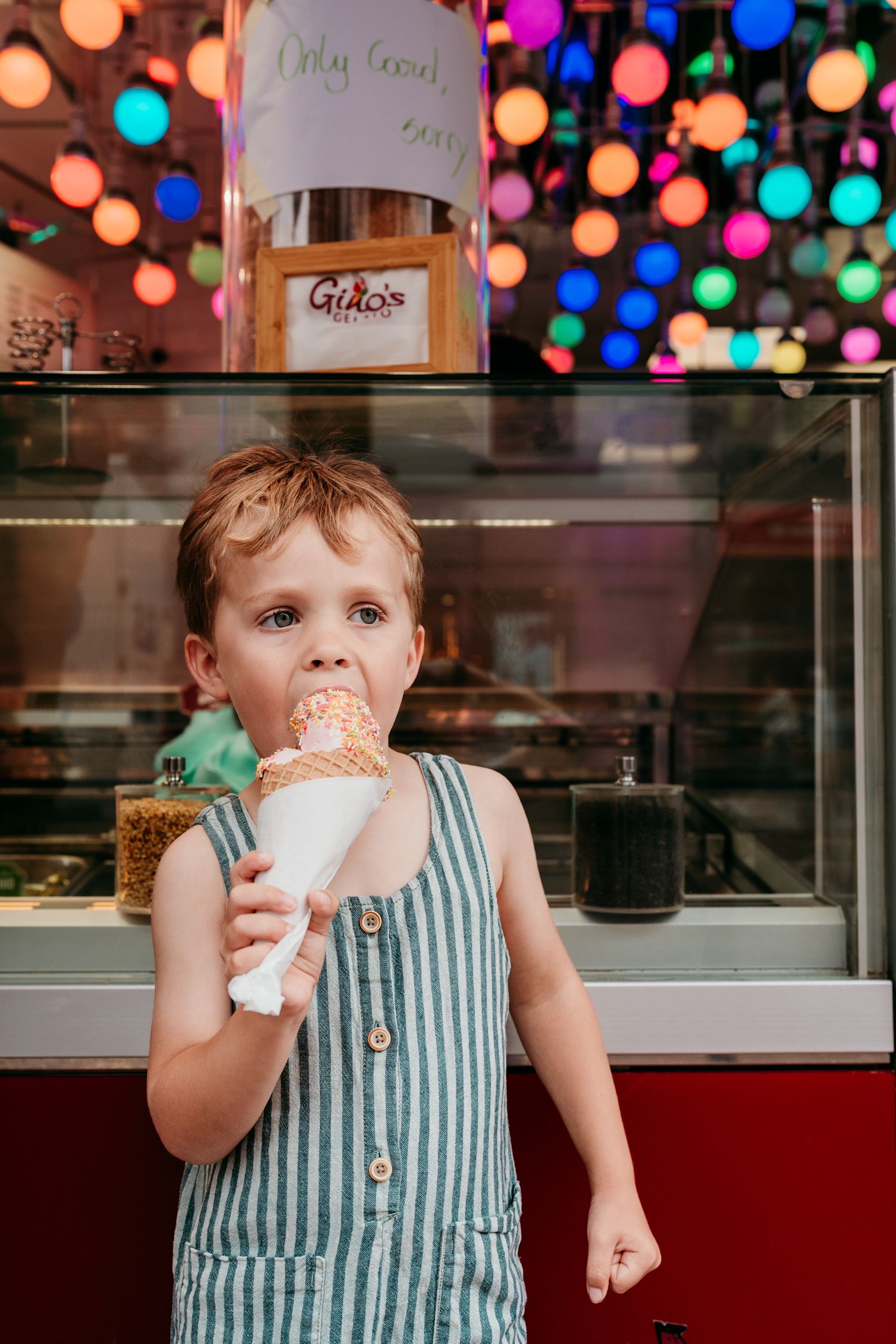 Young child enjoying an ice cream cone at night with colorful bokeh lights in the background.