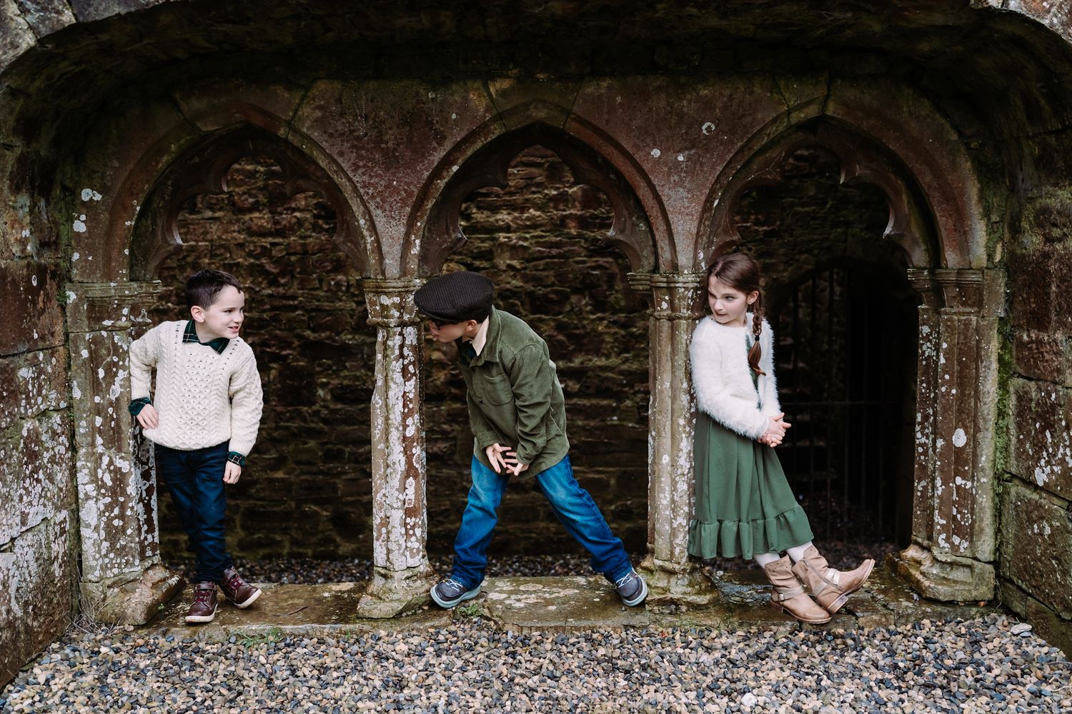 Three people pose together dramatically in stone archways of an old rustic building wall in moody lighting.